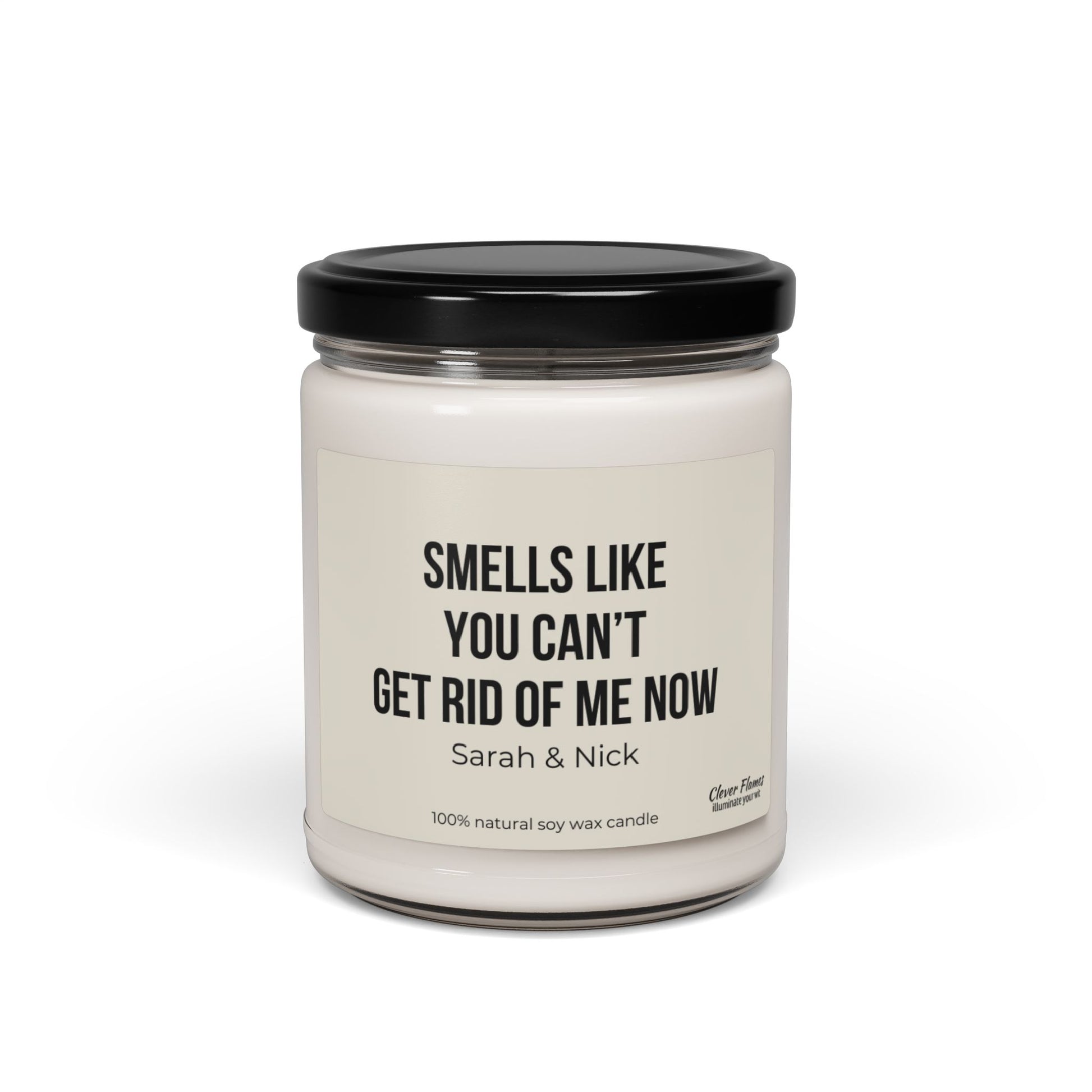 This personalized anniversary gift features a white scented candle made from natural soy wax, enclosed in a glass jar with a black lid. The label humorously states, "Smells like you can’t get rid of me now - Sarah & Nick," making it an ideal choice. Brought to you by Printify, it's perfect for friends, husbands, wives, birthdays, Valentine's Day, or as a best friend gift for him or her.