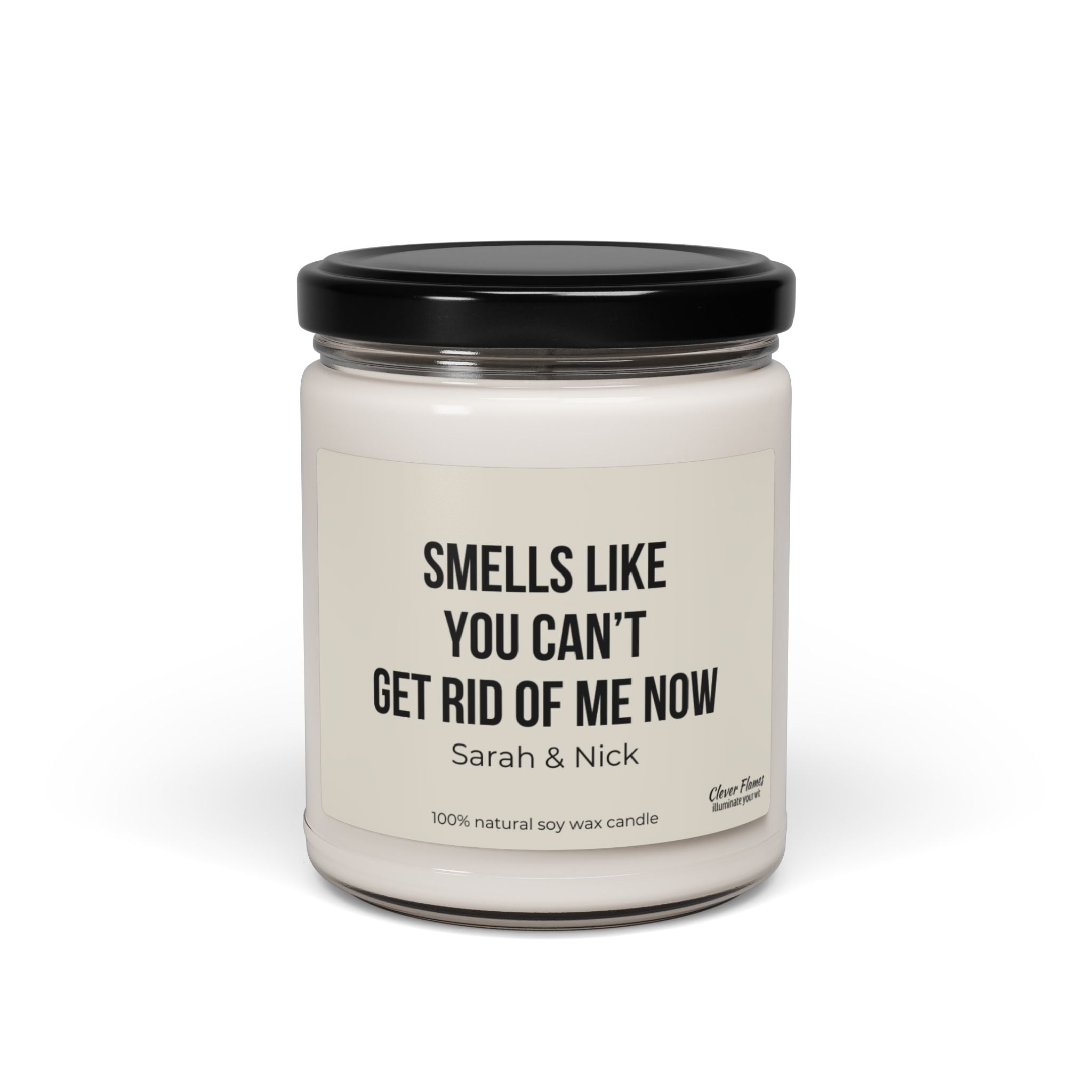 This personalized anniversary gift features a white scented candle made from natural soy wax, enclosed in a glass jar with a black lid. The label humorously states, "Smells like you can’t get rid of me now - Sarah & Nick," making it an ideal choice. Brought to you by Printify, it's perfect for friends, husbands, wives, birthdays, Valentine's Day, or as a best friend gift for him or her.