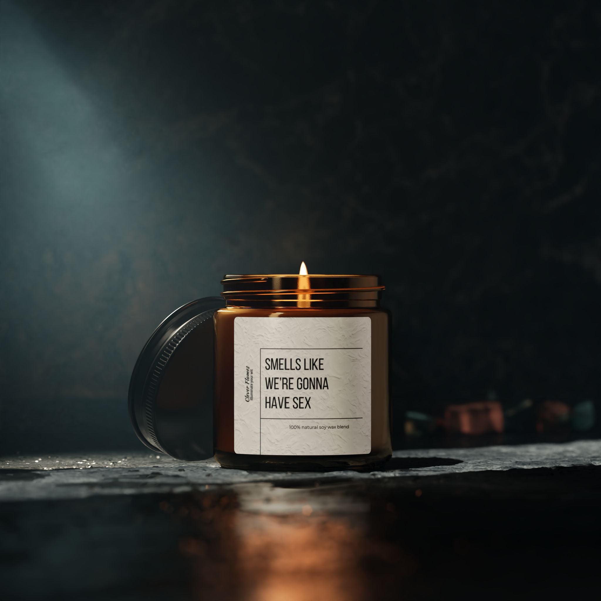 The Printify candle, Smells Like Were Gonna Have Sex, glows warmly in an amber jar on a textured surface. Its reusable glass vessel enhances its eco-friendly vibe, while the dark background creates a moody and intimate atmosphere.