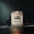 A lit Grandma Pregnancy Announcement Candle with its black lid nearby, featuring a label that reads Its Giving Grandma, February 2027, and Baby Smith for a personalized pregnancy announcement.