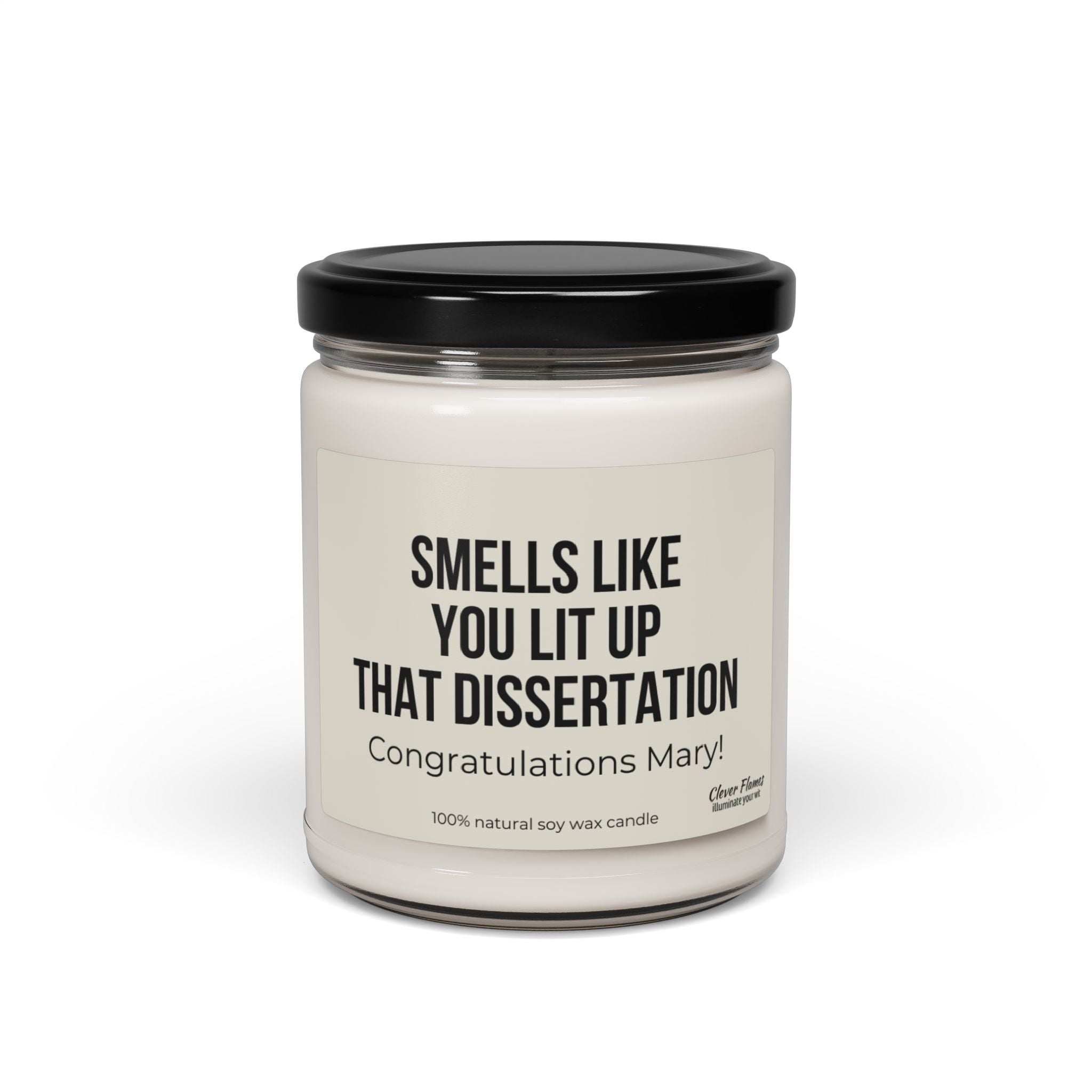 A personalized candle by Printify, featuring a white wax encased in a glass jar with a black lid. The label reads, "Smells like you lit up that dissertation. Congratulations Mary!" Made from 100% natural soy wax, this 'Smells Like You Lit Up That Dissertation' candle makes an ideal graduation gift for future doctors.