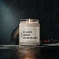 The Printify My Favorite Daughter Scented Soy Candle, 9oz, with a labeled glass jar and black lid, sits lit on a dark surface against a blurred background—ideal for birthdays, Mother’s Day, decor, relaxation, or celebrations.