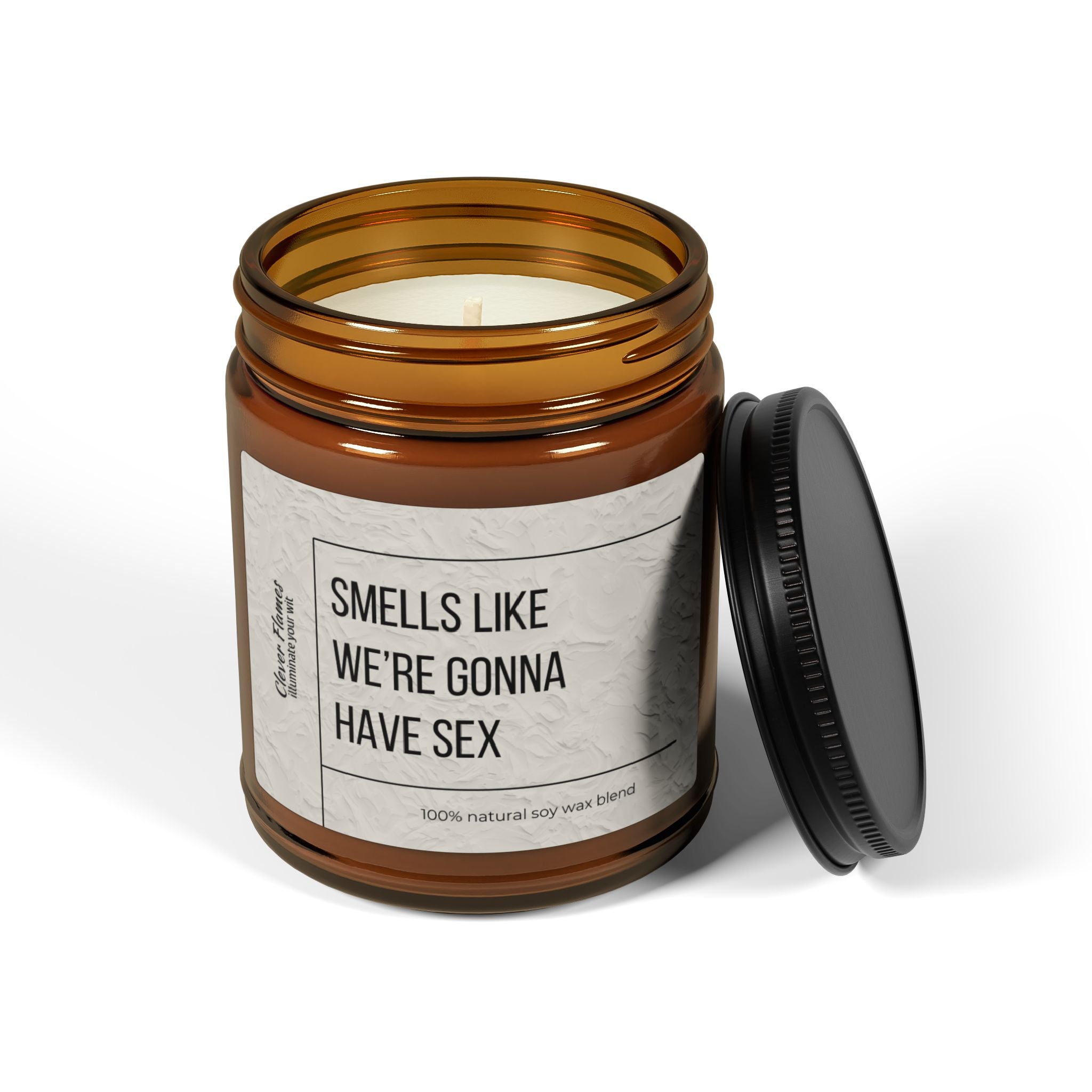 The Printify candle, labeled Smells Like Were Gonna Have Sex, has a brown vessel with a black lid beside it. Made from 100% natural soy wax and presented in a reusable glass jar, its minimalistic design and bold label promise intimacy and modern eco-friendliness.