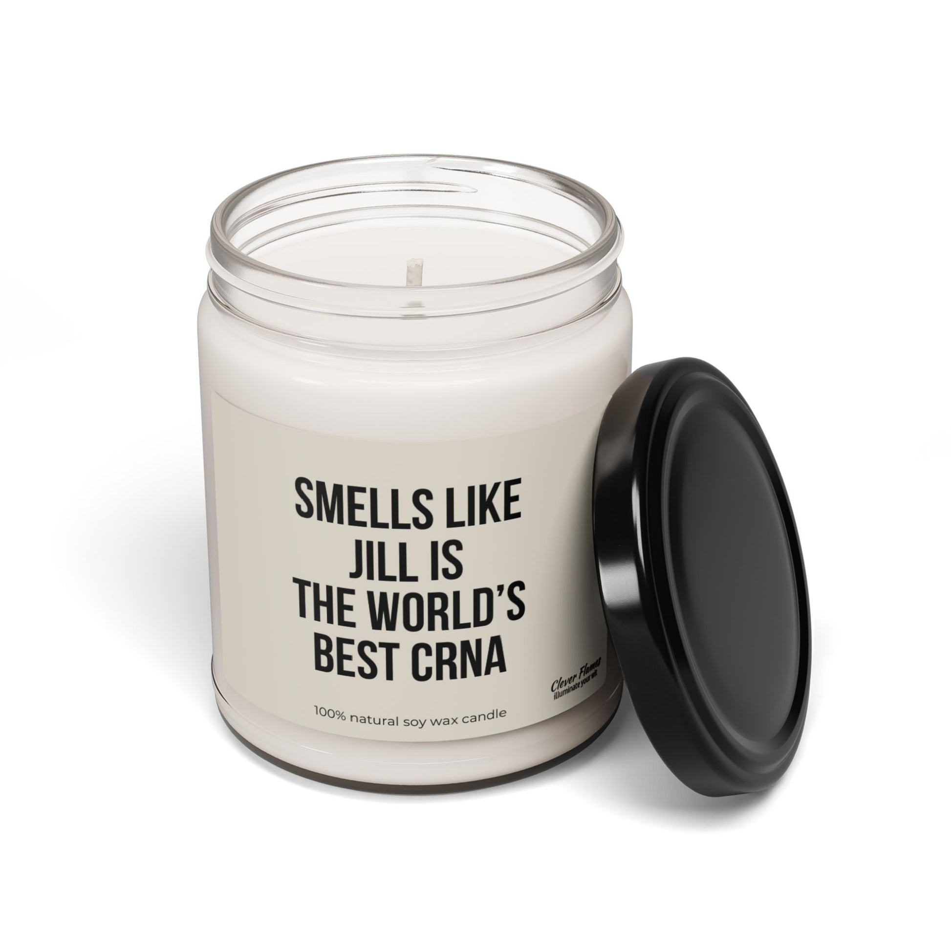 A glass jar holds a white candle accompanied by a black lid, labeled "Smells like Jill is the world's best CRNA." This personalized candle from Printify, crafted with 100% natural soy wax, serves as an excellent gift for nurse anesthetists.