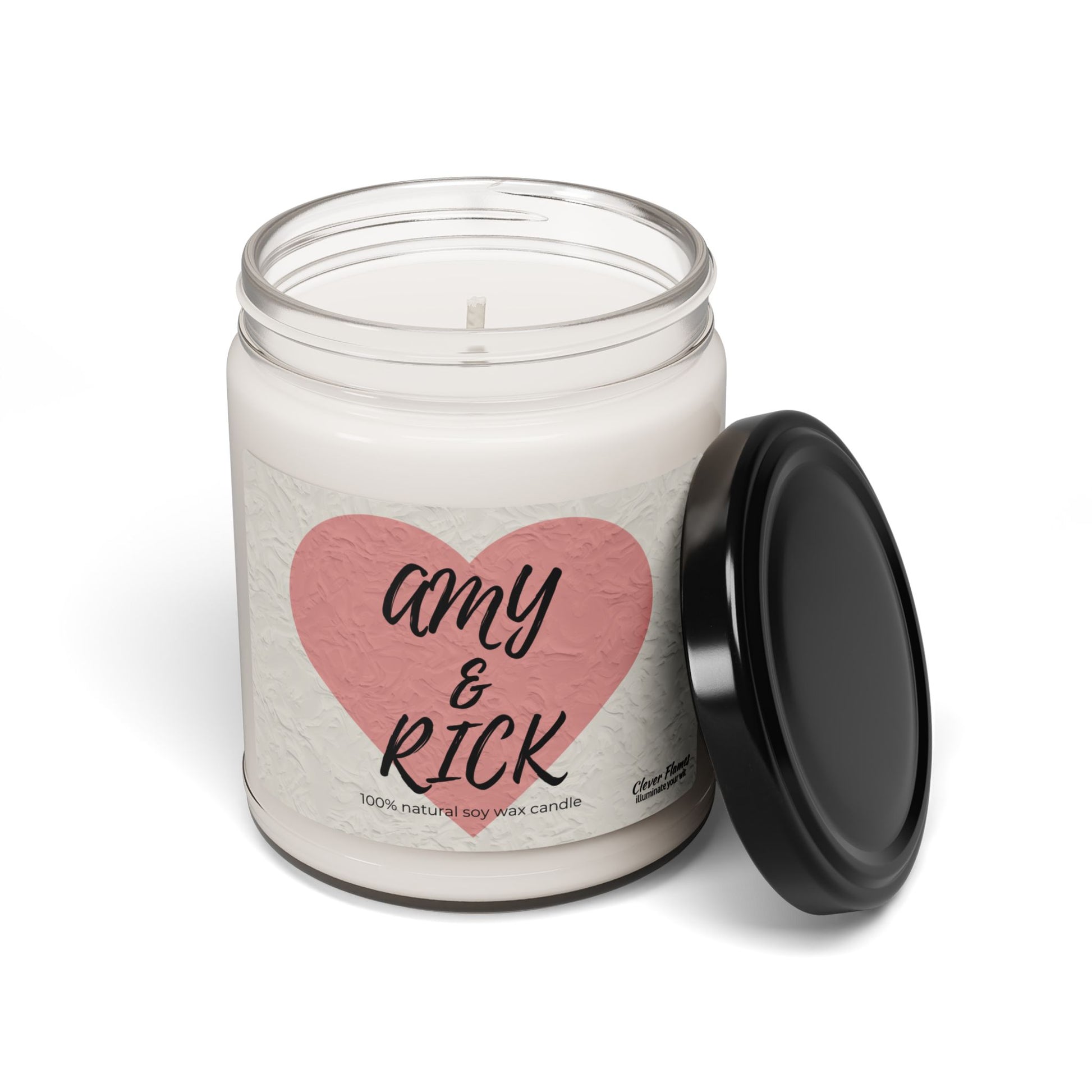 A white jar candle with a black lid rests on its side, showcasing a pink heart with Amy & Rick in stylish black script. Below, it reads 100% natural soy wax candle. Printify offers this Personalized Couples Candle as the perfect custom romantic gift and keepsake for special occasions.