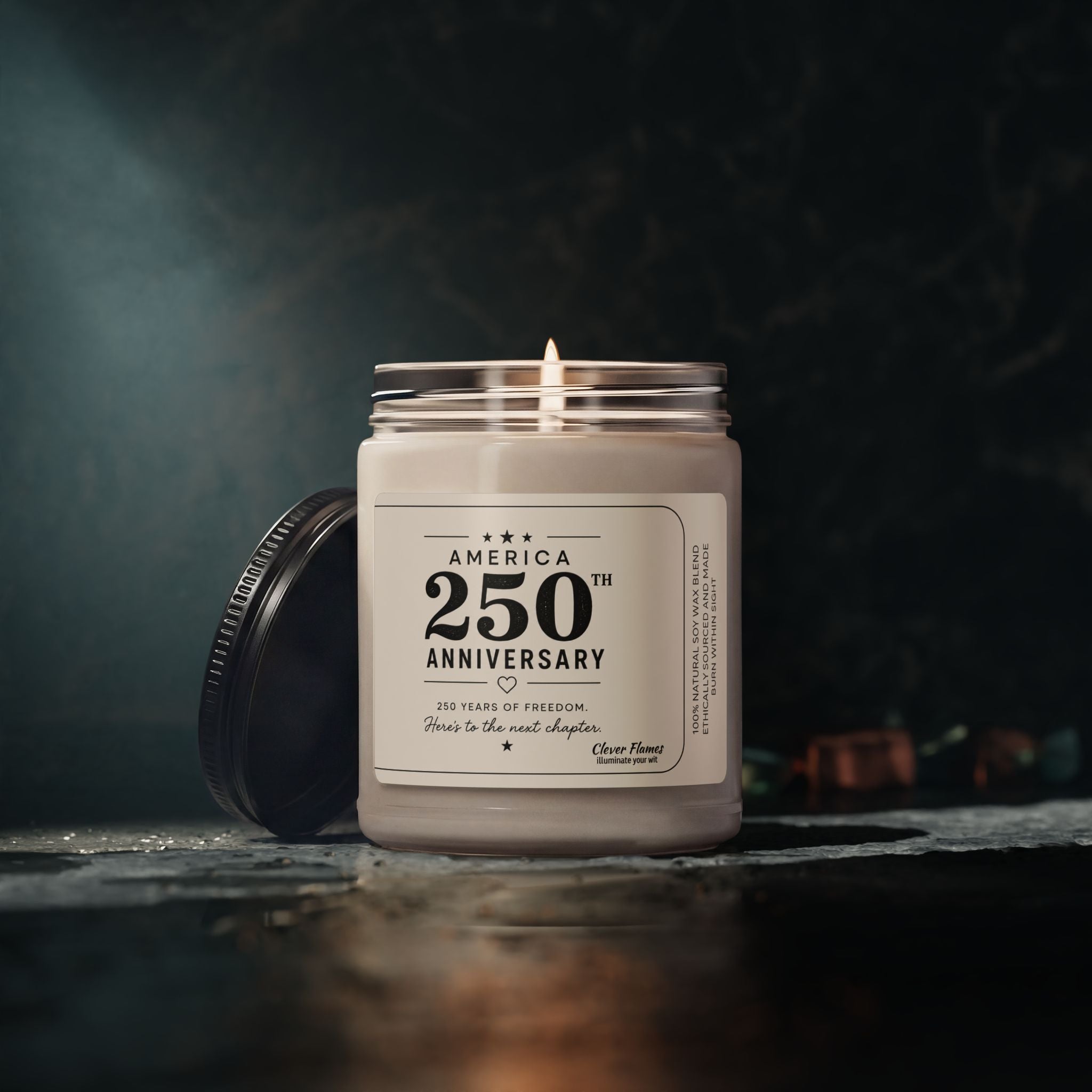 The Printify America 250th Anniversary Scented Soy Candle, 9oz, features a patriotic label and a removable black lid—perfect as a Semiquincentennial gift or for displaying your love of freedom. Shown lit in its glass jar against a dark, blurred background.