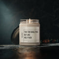 The 9oz Humorous Scented Soy Candle from Printify, labeled This Too Shall Pass, But Like Holy F***, sits in a glass jar with the lid beside it on a dark textured surface against a moody backdrop.