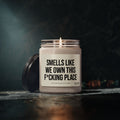 A lit Smells Like We Own This F*Cking Place Candle in a glass jar, making a funny housewarming gift for a new homeowner.