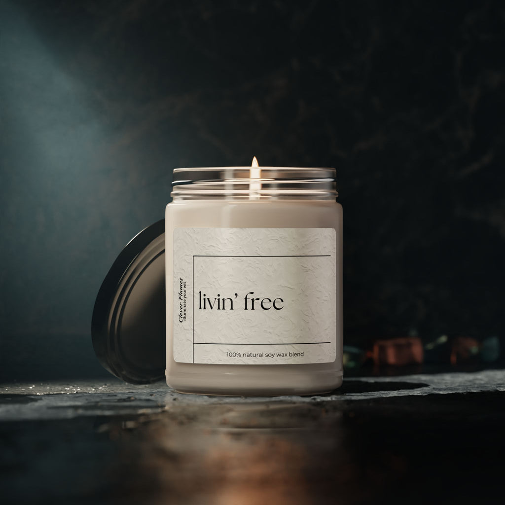 A Livin’ Free Summer Break Candle by Printify, made with natural soy wax in a glass jar, glows softly on a dark surface—perfect as a funny teacher appreciation gift for summer vacation lovers. Cozy, blurred background enhances its charm.