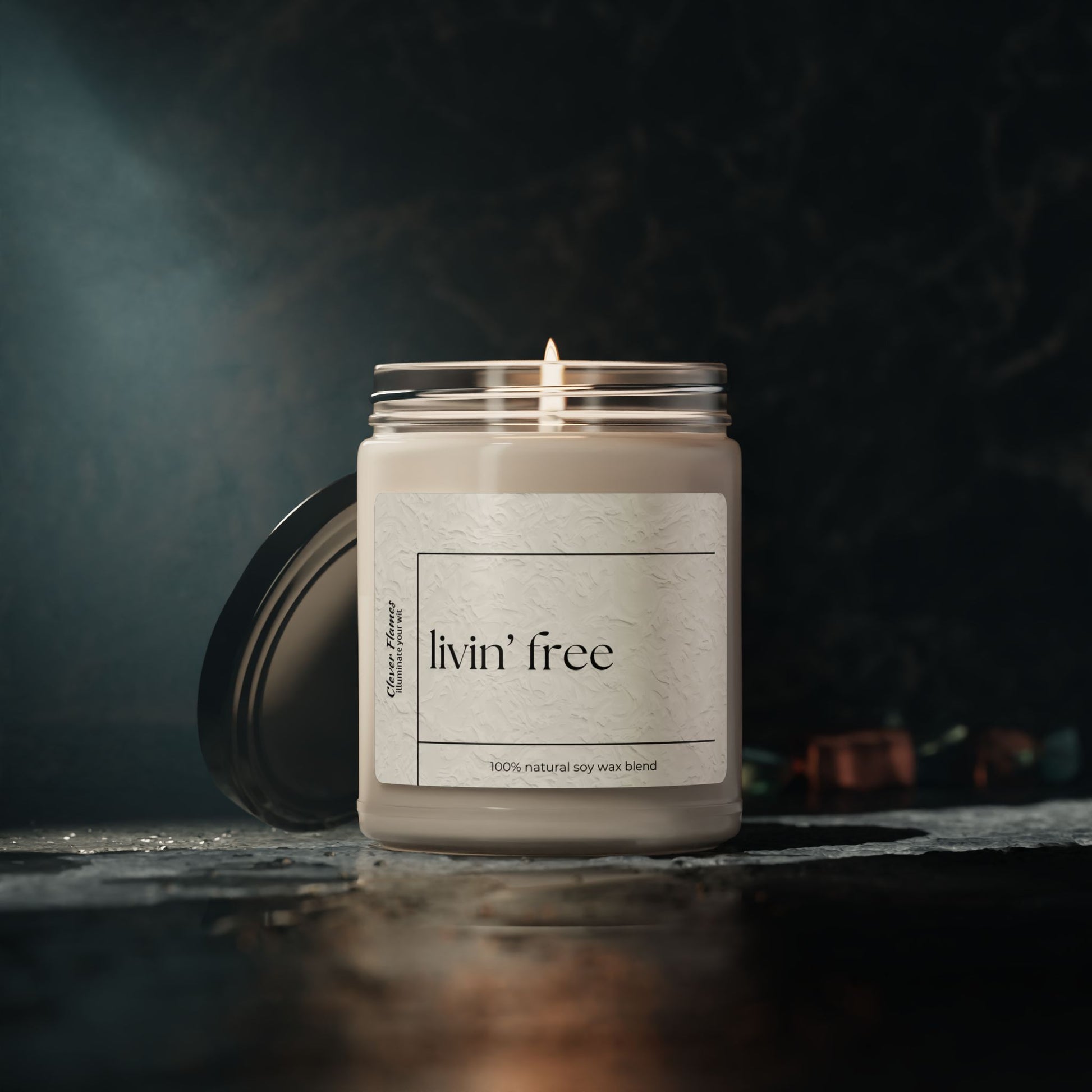 A Livin’ Free Summer Break Candle by Printify, made with natural soy wax in a glass jar, glows softly on a dark surface—perfect as a funny teacher appreciation gift for summer vacation lovers. Cozy, blurred background enhances its charm.