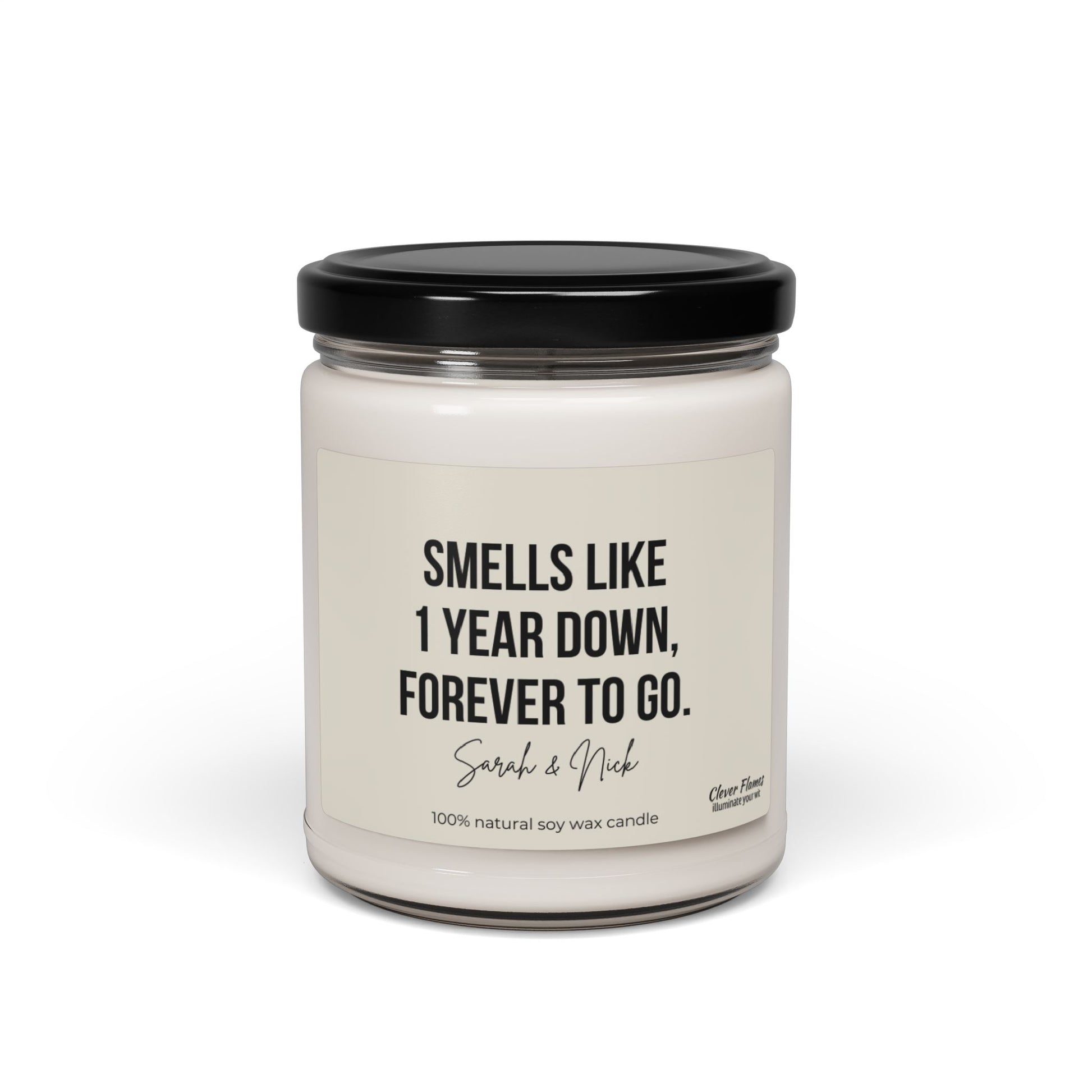 Introducing the Wedding brand's personalized anniversary candle: a white, scented soy candle housed in a glass jar with a black lid. The label lovingly declares, "Smells like 1 year down, forever to go," featuring the names Sarah & Nick. Crafted from 100% natural soy wax, this unique candle is an ideal gift for celebrating your first anniversary.