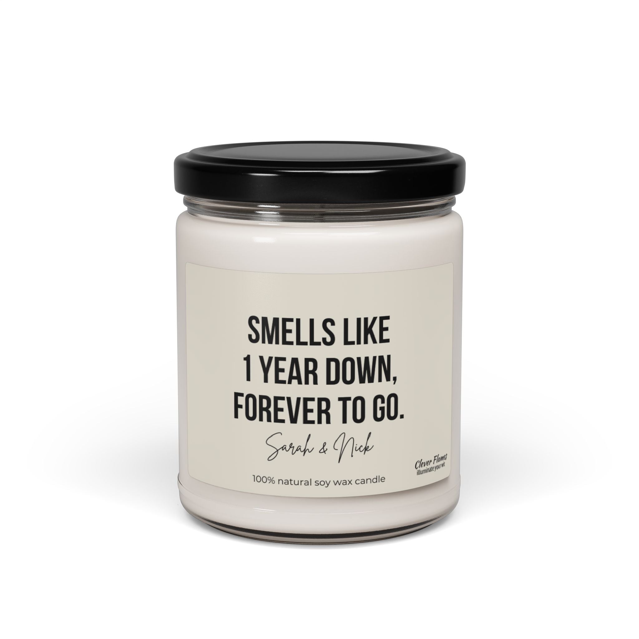 Introducing the Wedding brand's personalized anniversary candle: a white, scented soy candle housed in a glass jar with a black lid. The label lovingly declares, "Smells like 1 year down, forever to go," featuring the names Sarah & Nick. Crafted from 100% natural soy wax, this unique candle is an ideal gift for celebrating your first anniversary.
