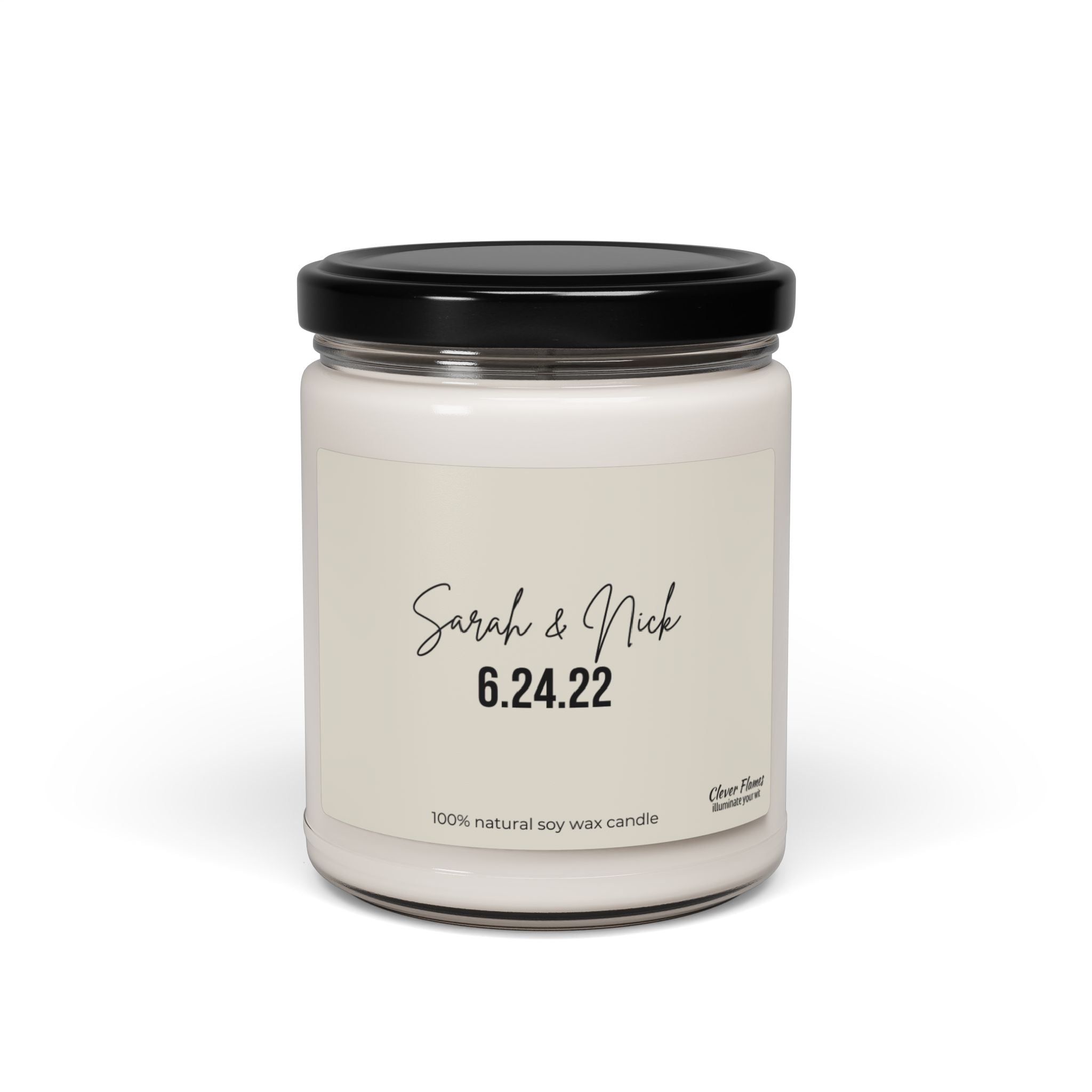 A personalized wedding gift candle in a clear jar with a black lid exudes elegance. The label displays "Sarah & Nick 6.24.22" and "100% natural soy wax candle," seamlessly integrating with its minimalist design. Crafted by Wedding, this custom candle is perfect for celebrating cherished moments.