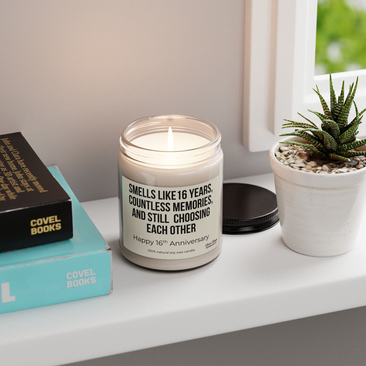 A 16th Anniversary Candle by Printify, a romantic wax anniversary gift for wife or husband, glows in a glass jar on the windowsill beside a potted succulent and books. The label reads: Smells like 16 years, countless memories, and still choosing each other.