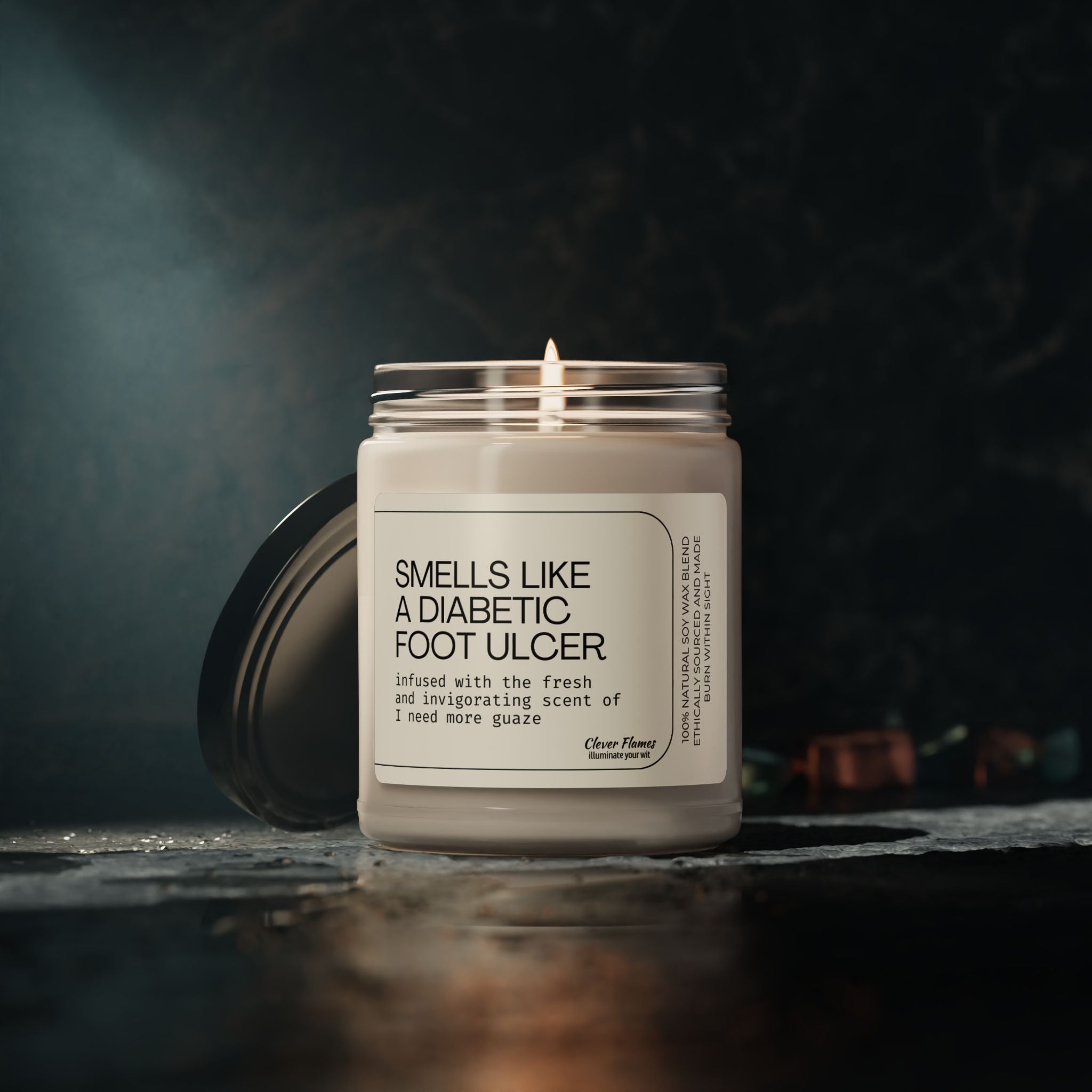 A lit candle in a glass jar sits on a dark surface labeled Printify: Funny Wound Care Nurse Candle – Smells Like a Diabetic Foot Ulcer. It offers a fresh scent and amusing phrases, ideal for medical humor gifts or bringing smiles to wound care nurses. The background is dimly lit.