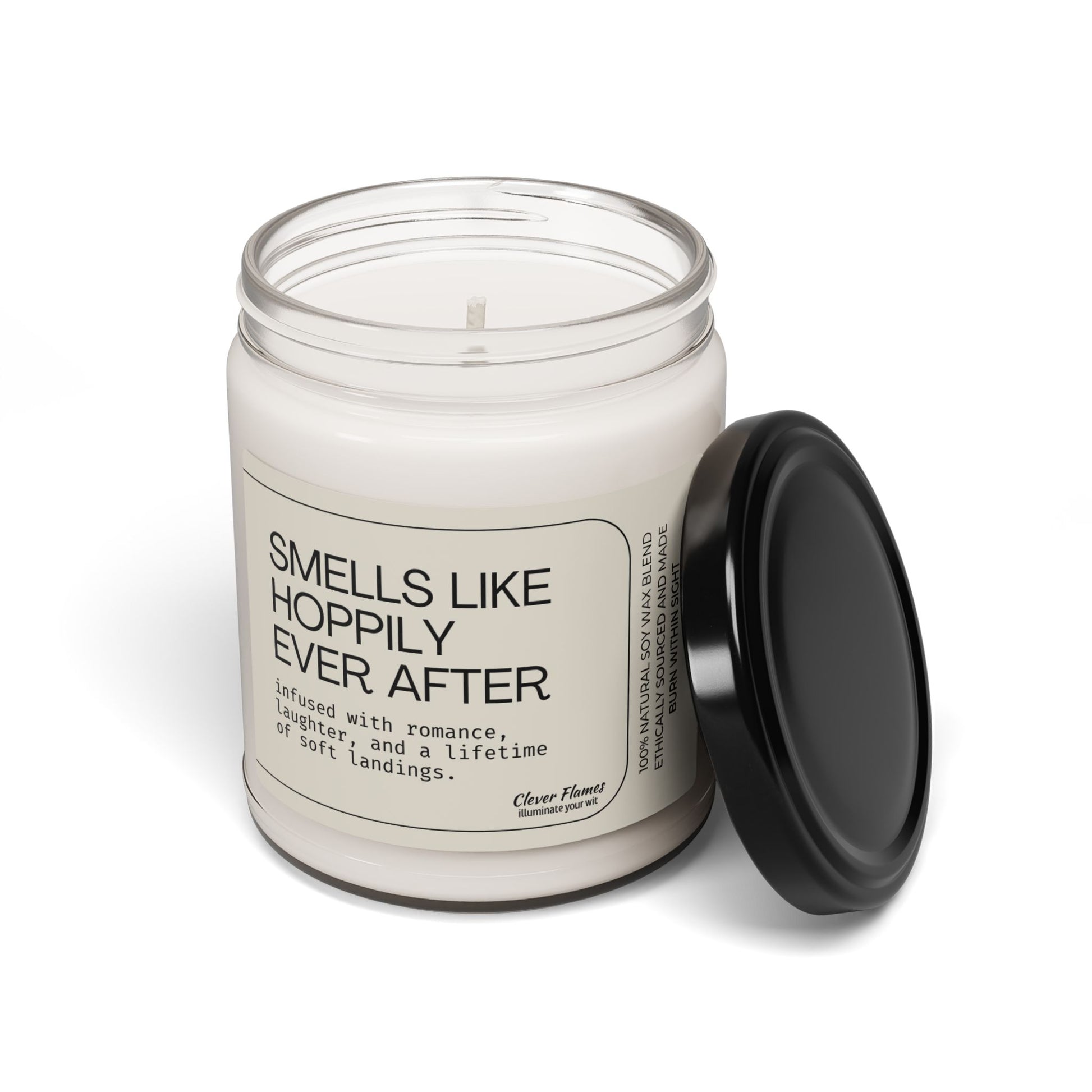 A white vegan soy wax candle by Printify, called "Smells Like Hoppily Ever After," sits in a glass jar with a black lid. This Clever Flames candle makes a funny, romantic wedding or anniversary gift, perfect for celebrating love and laughter.