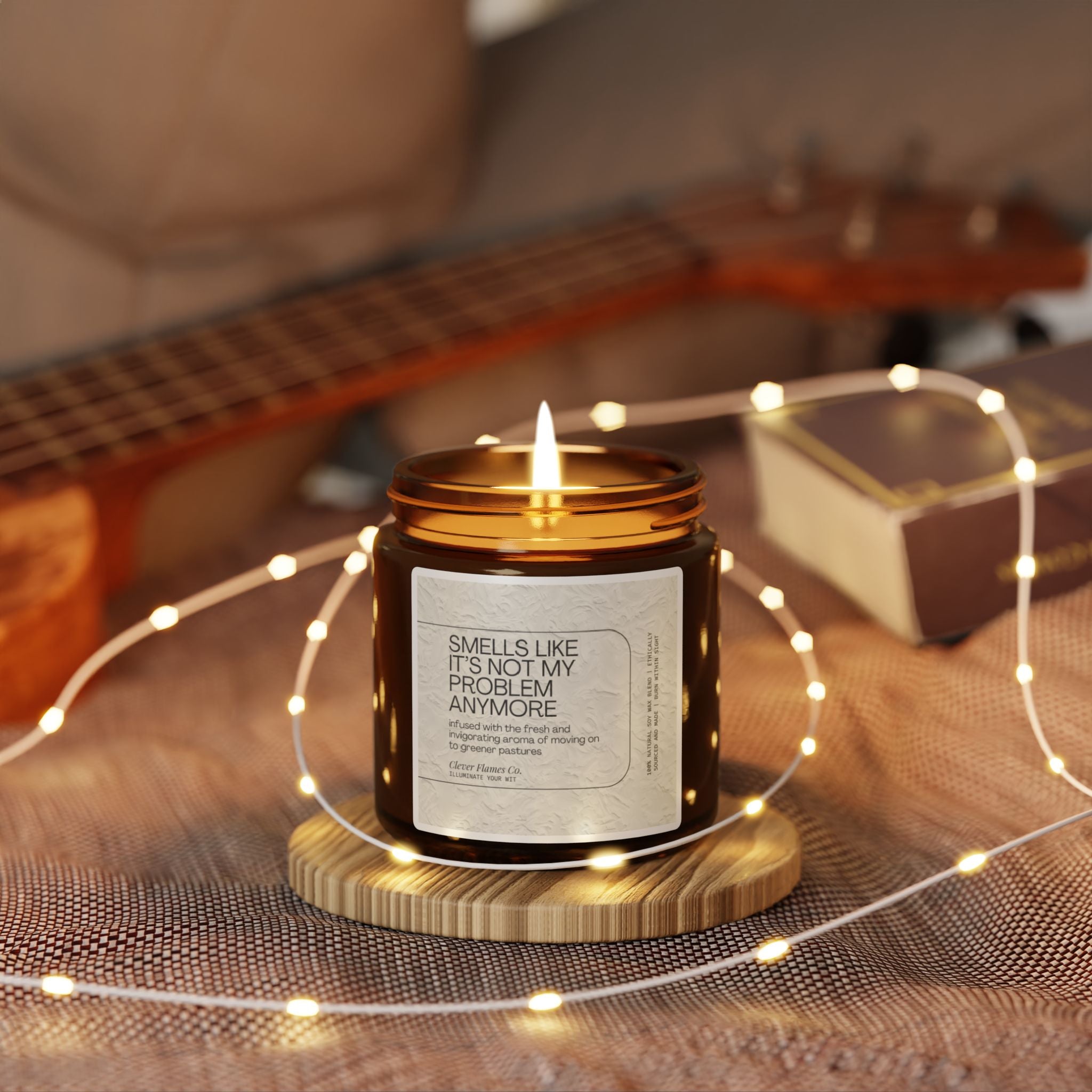 A Funny Retirement Scented Soy Candle by Printify, labeled "Not My Problem Anymore," sits on a wooden coaster. The soft lighting enhances a cozy atmosphere, with a blurred background showcasing a guitar and string lights, creating a warm and relaxed setting—an ideal whimsical farewell gift.
