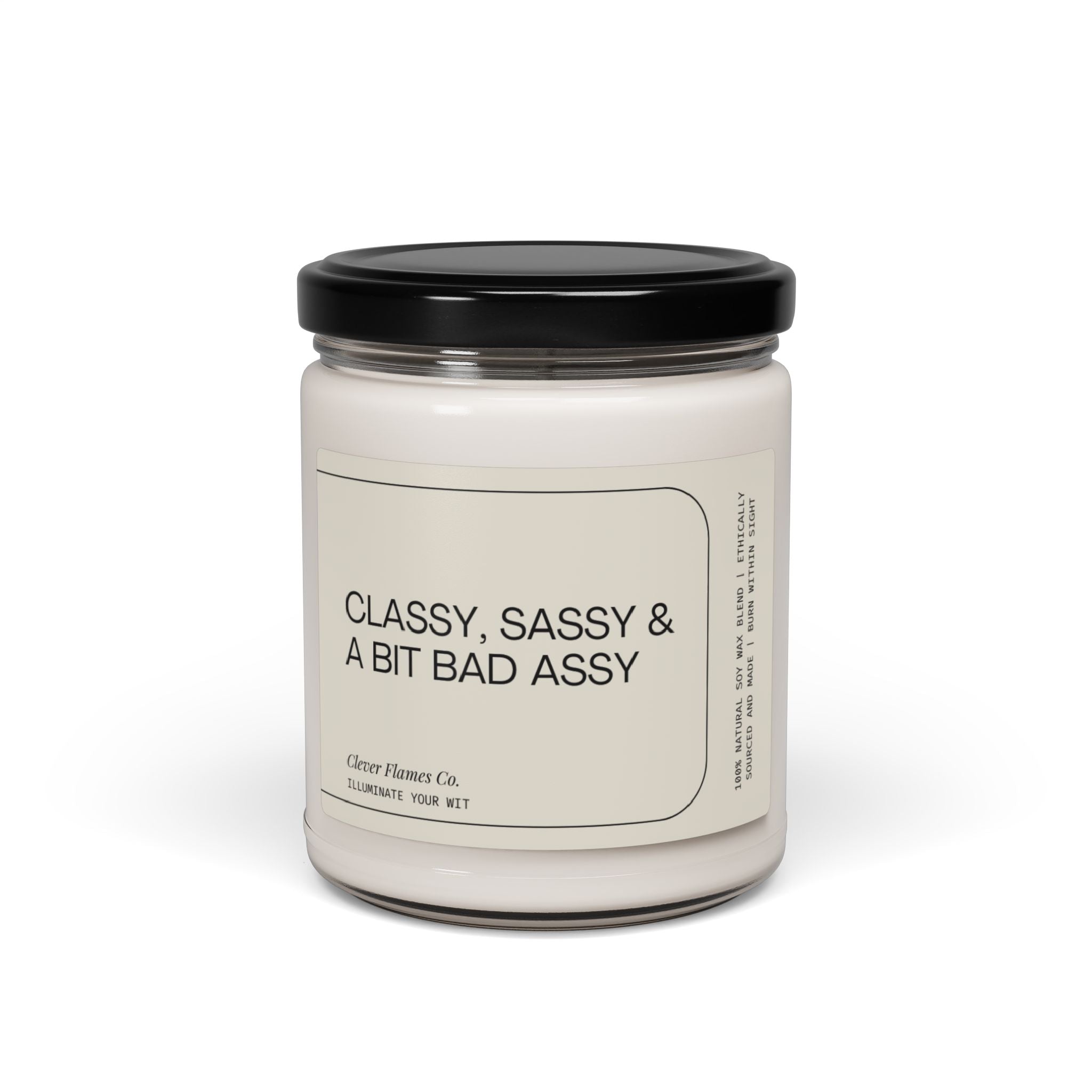 A white soy candle in a glass jar with a black lid is labeled "CLASSY, SASSY & A BIT BAD ASSY." Crafted from natural soy wax and featuring a cotton wick, it prominently displays the brand name Printify.