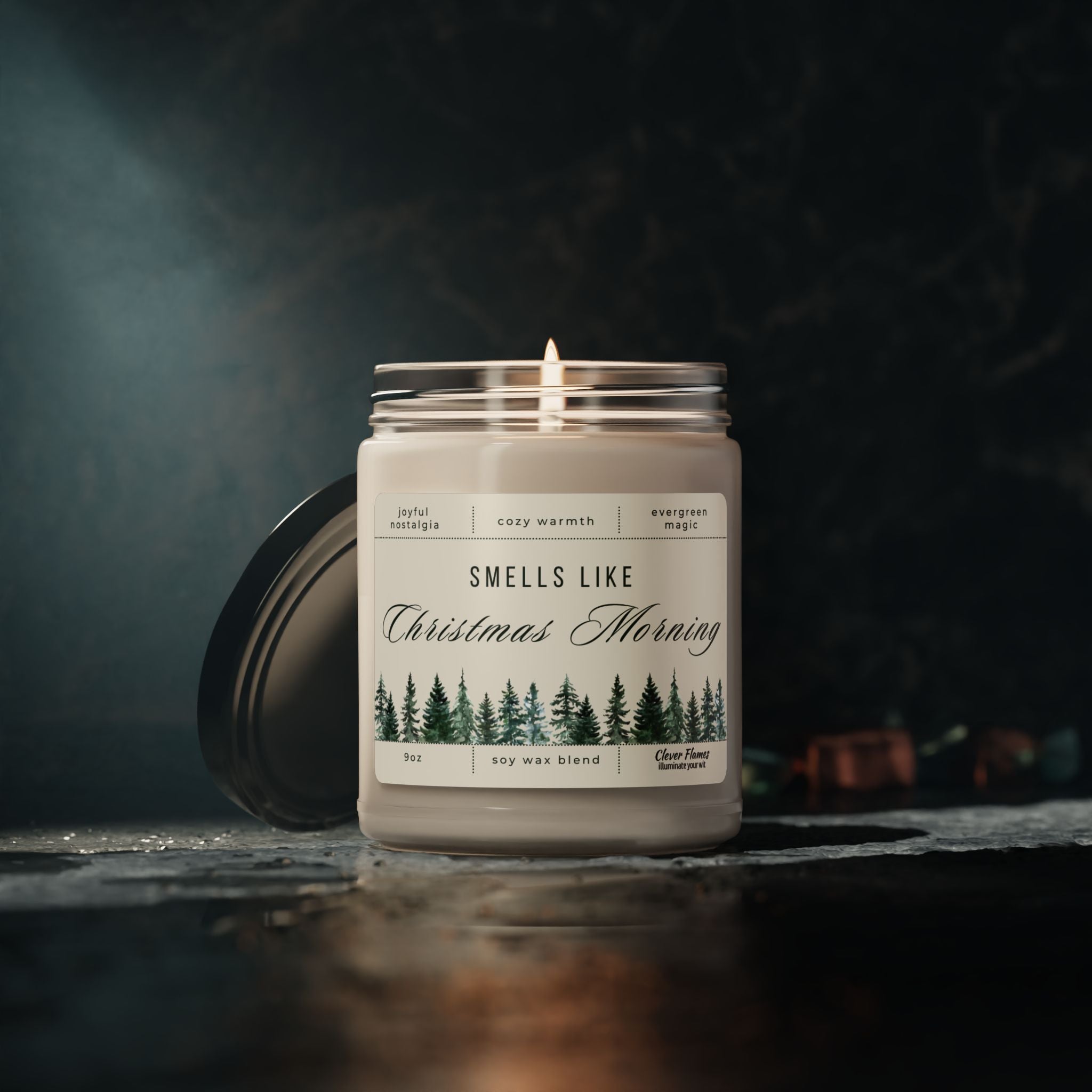 A 9oz Smells Like Christmas Morning – Holiday Soy Candle by Printify glows in a glass jar with pine tree illustrations and its black lid beside it, creating a cozy holiday atmosphere against a dark surface and blurred background.