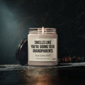 A 9oz “You’re Going to Be Grandparents – Personalized Pregnancy Announcement Candle” by Printify sits in a glass jar labeled, “Smells like you’re going to be grandparents. Due June 2027.” Its lid rests beside it on a dark surface, making this personalized candle the perfect grandparent gift or baby reveal idea.