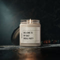 A lit Printify Welcome to My Cult Bridal Party Scented Soy Candle (9oz) sits in a glass jar with its lid beside it on a dark surface. The dim, blurred background highlights this eco-friendly candle and its unique scents.