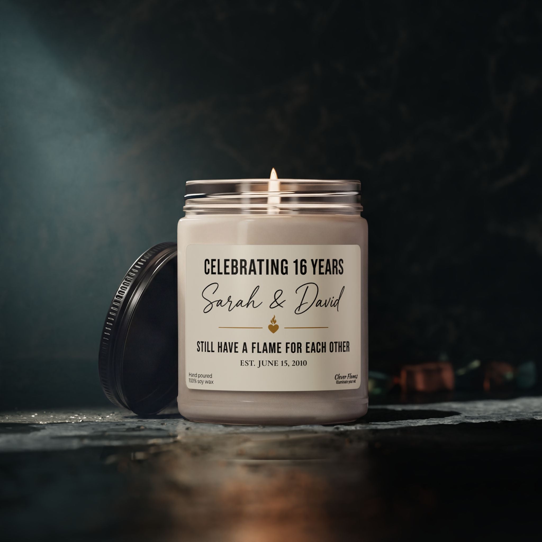 A personalized 16th Anniversary Candle by Printify, this elegant white candle comes in a glass jar featuring a custom label: “Celebrating 16 Years, Sarah & David, Still Have a Flame for Each Other, Est. June 15, 2010.” With the candle aglow and its lid beside it, this custom wax anniversary gift is a thoughtful way to honor 16 years of marriage—a heartfelt present for your wife or husband to celebrate enduring love.