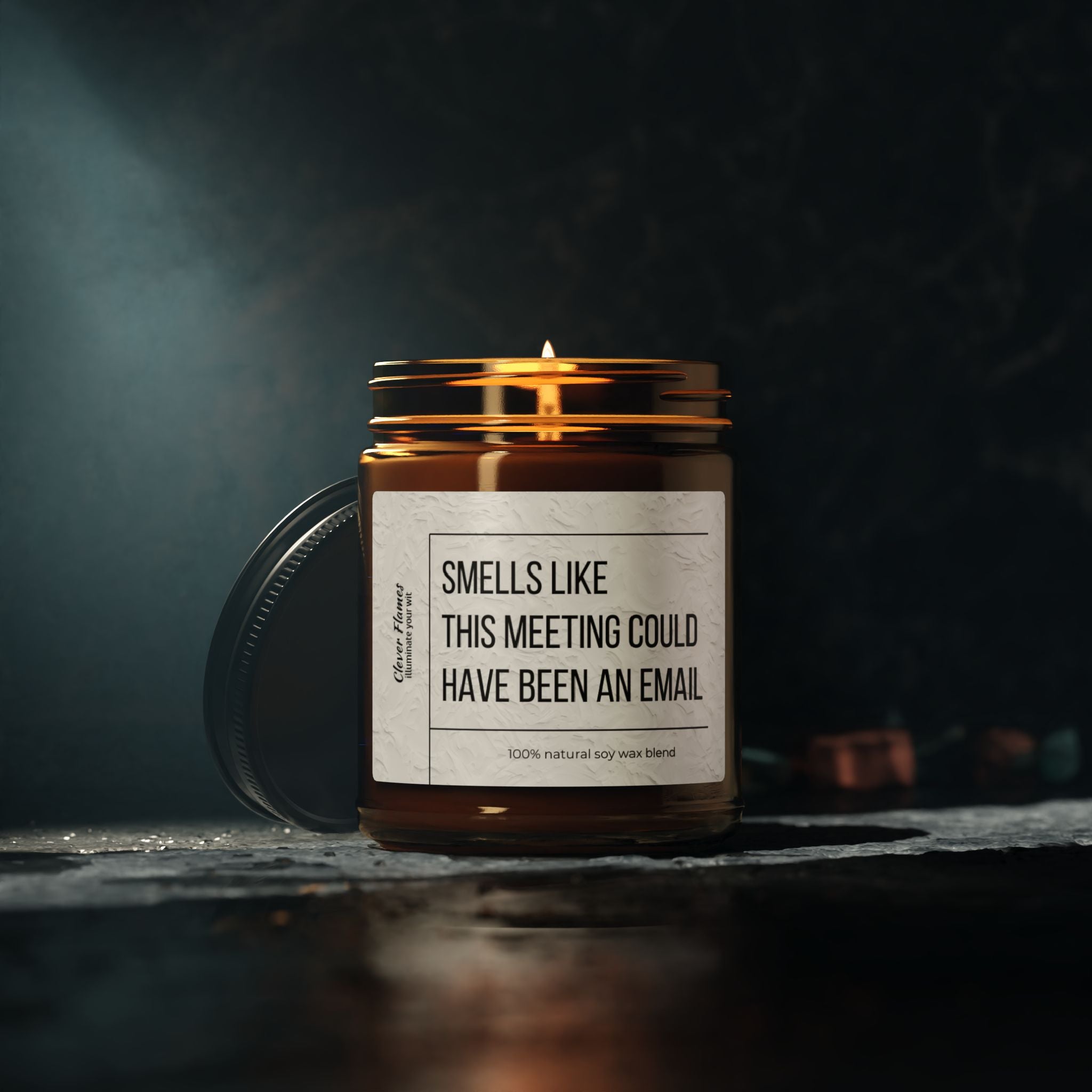 A lit brown soy candle from Printify, humorously labeled "Smells like this meeting could have been an email," fills a dark room with its scent while resting on a stone surface against a blurred background. This eco-friendly treasure is an ideal gift for bosses, bringing both humor and ambiance to any environment.