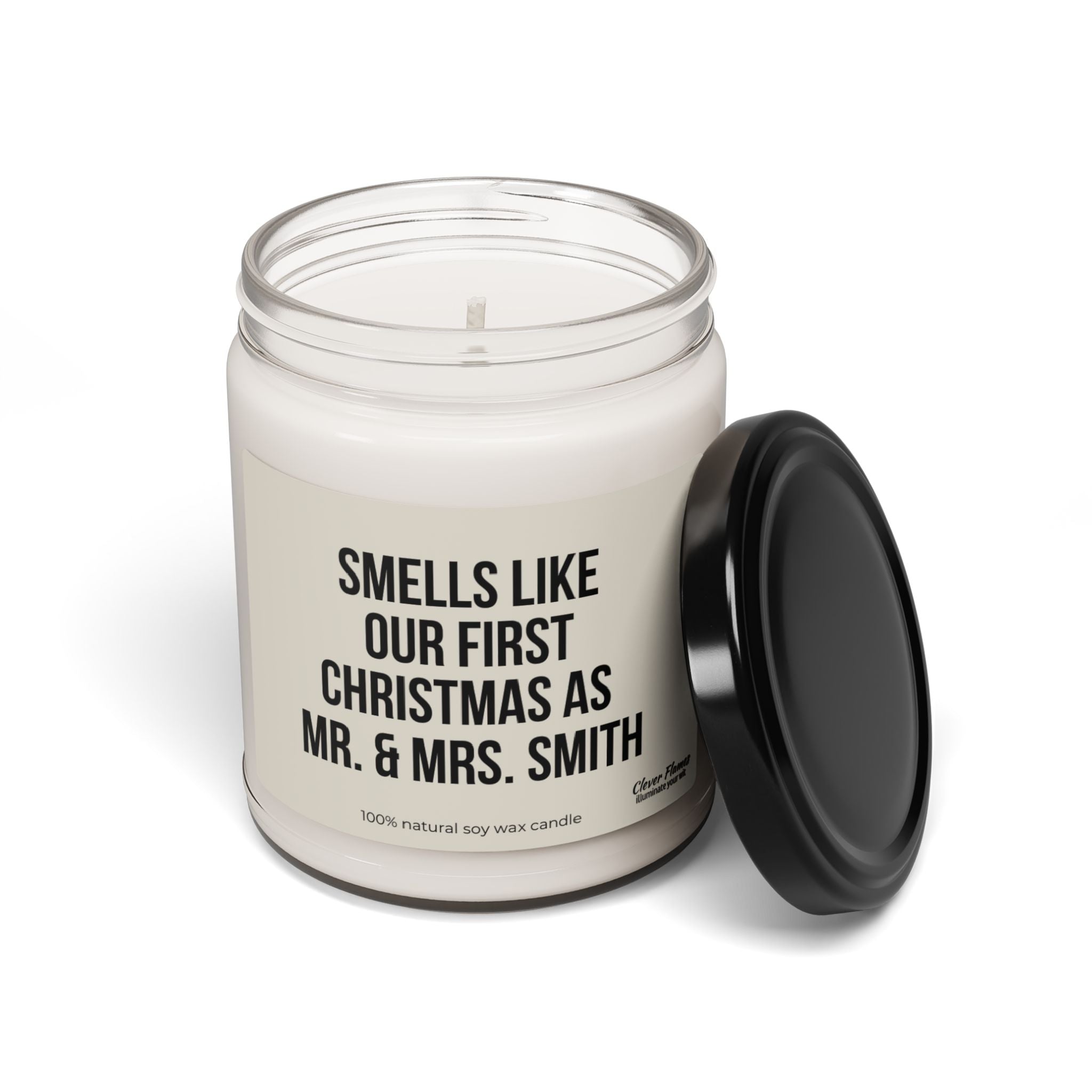 A white candle in a glass jar with a black lid, ideal as a gift for newlyweds. The label says, "Smells like our first Christmas as Mr. & Mrs. Smith." This personalized candle from Printify is made from 100% natural soy wax and is named "Personalized First Christmas as Mr and Mrs Candle for Newly Married Couple Gift for Just Married Couple for Her.