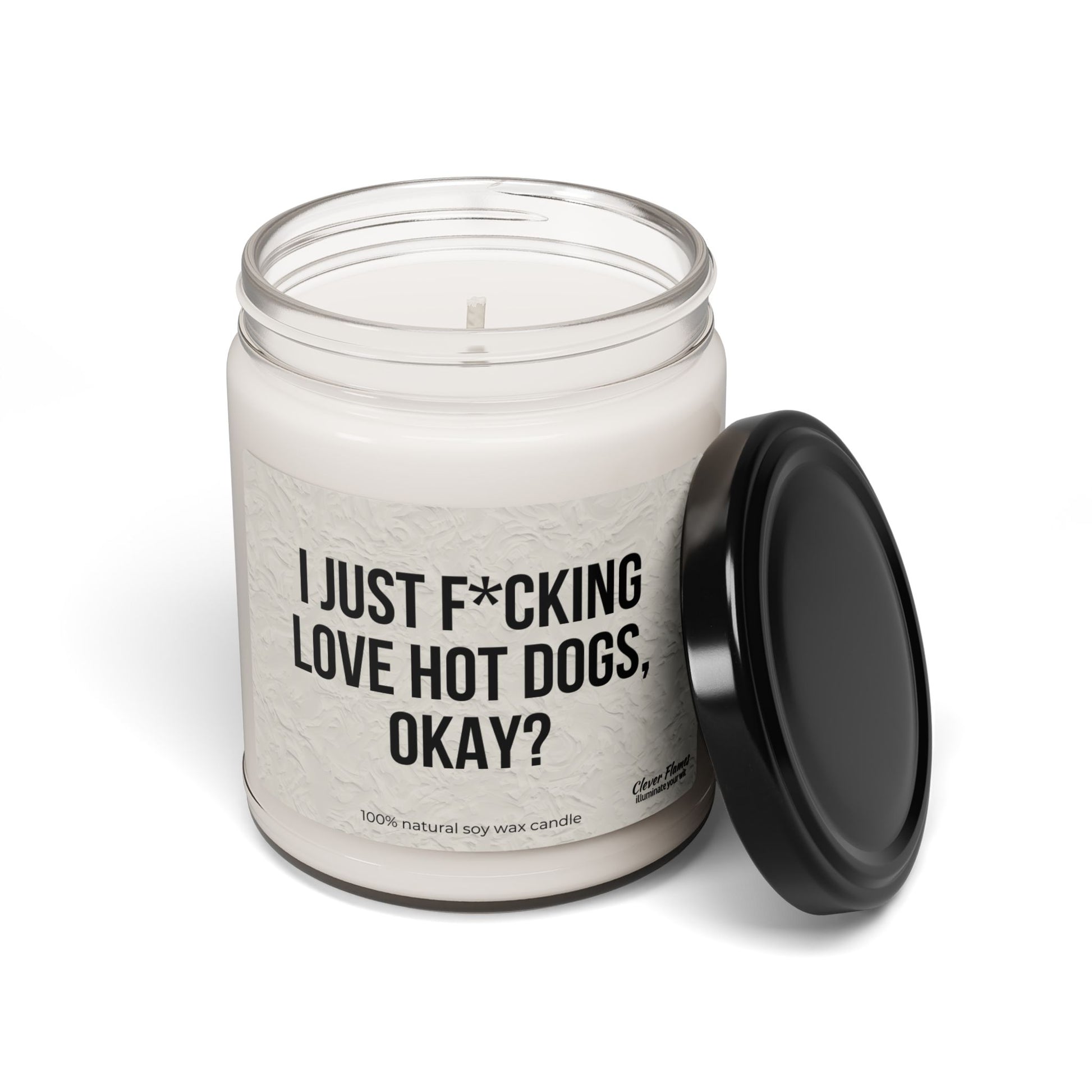 The Printify "I Just F*cking Love Hot Dogs Okay?" Candle is a 9oz scented soy candle in a reusable glass jar with black lid, featuring the bold phrase on its label.