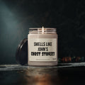 A lit Printify Personalized Ghost Stories Soy Halloween Candle Gift for Spooky Decor for Fall October Holiday Room sits in a glass jar on a dark surface, its lid resting nearby. The candle’s soft glow creates an eerie ambiance against the dim, blurred background—perfect for adding unique Halloween flair to your space.