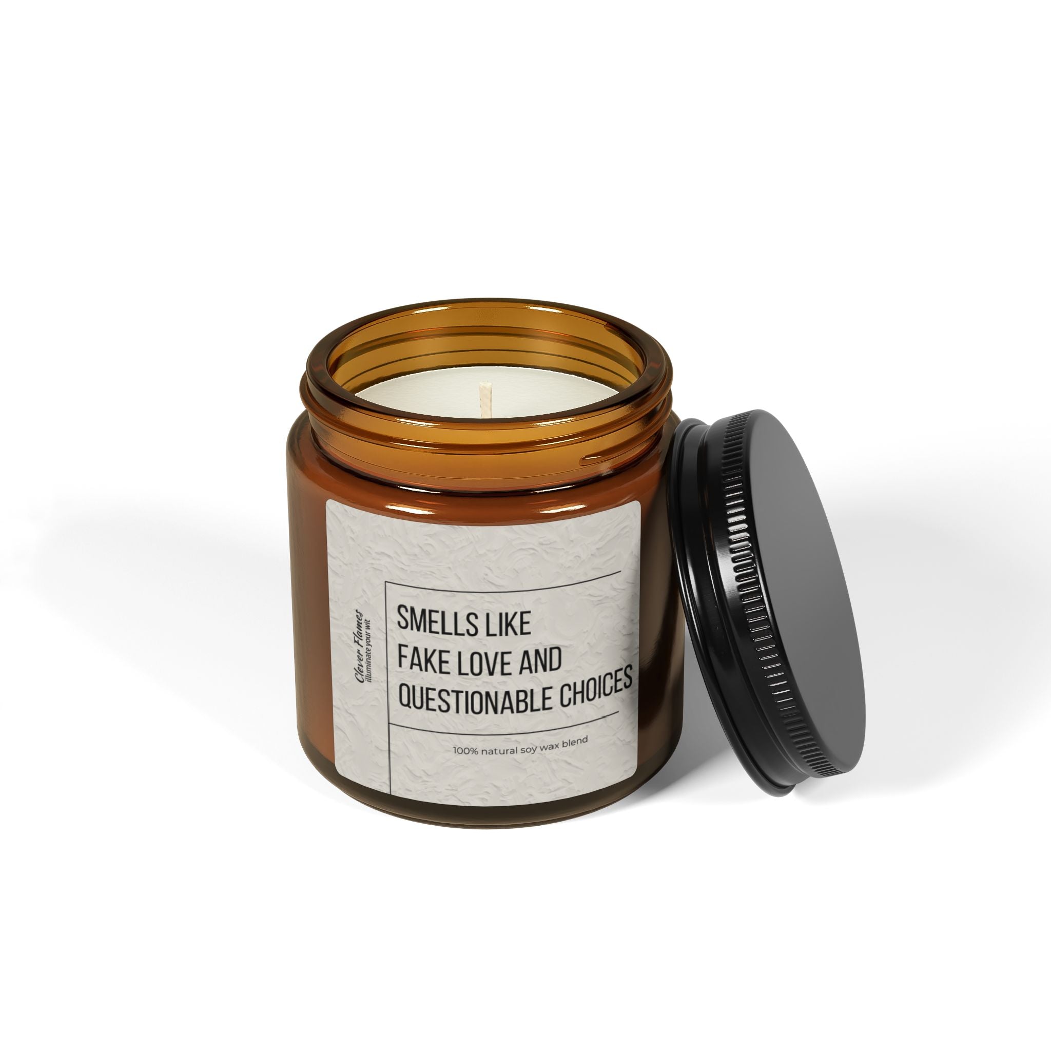 Beside it sits a Printify candle in a brown glass jar with a black lid, ideal for Valentines Day. Labeled humorously as Smells Like Fake Love and Questionable Choices, this scented soy candle appears unused with its pristine white wax and unlit wick.