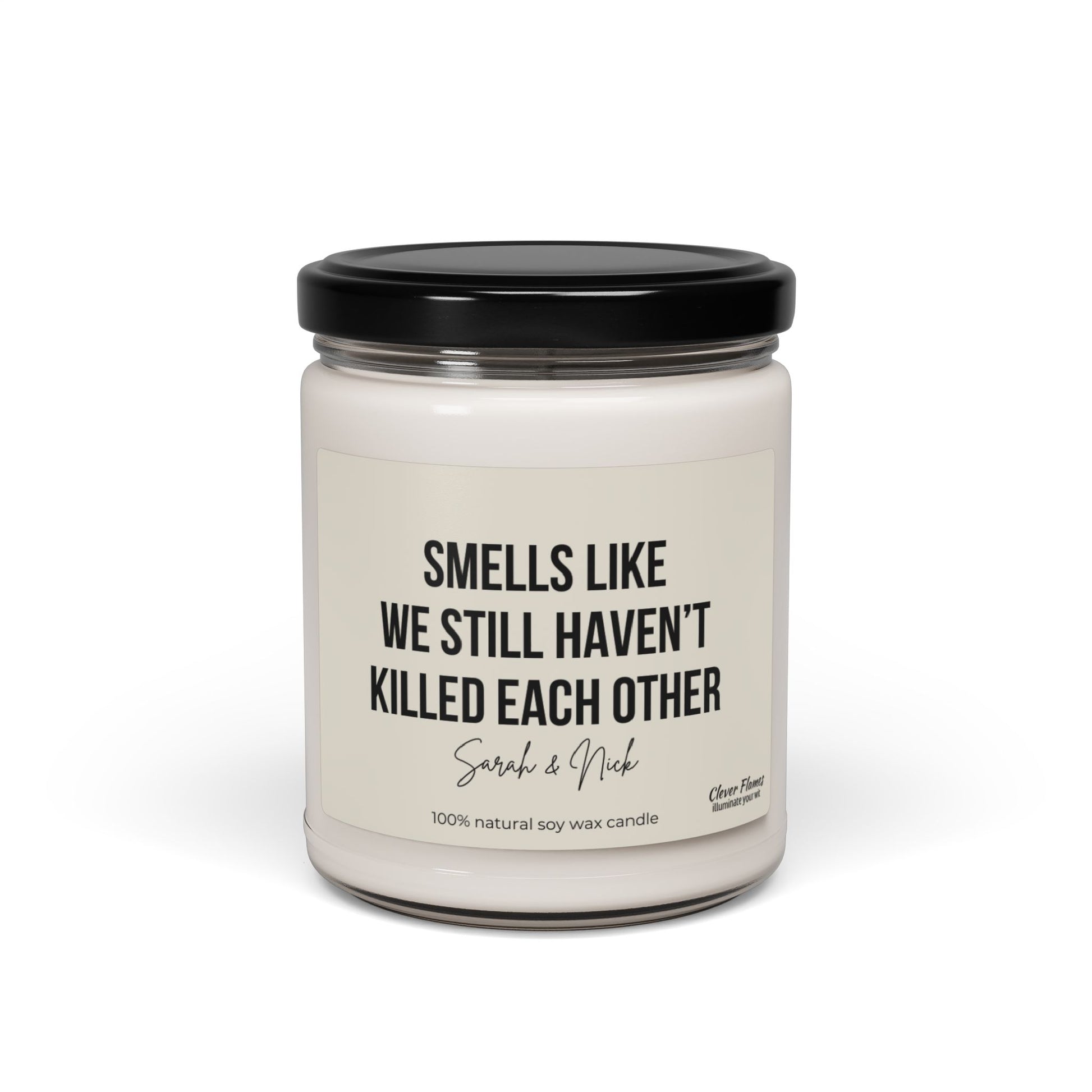 A personalized anniversary candle by Wedding, featuring a humorous message that reads "Smells like we still haven’t killed each other," is crafted from 100% natural soy wax. This white candle comes in a glass jar with a black lid and makes an excellent gift for friends, husbands, wives, birthdays, or Valentine's Day.
