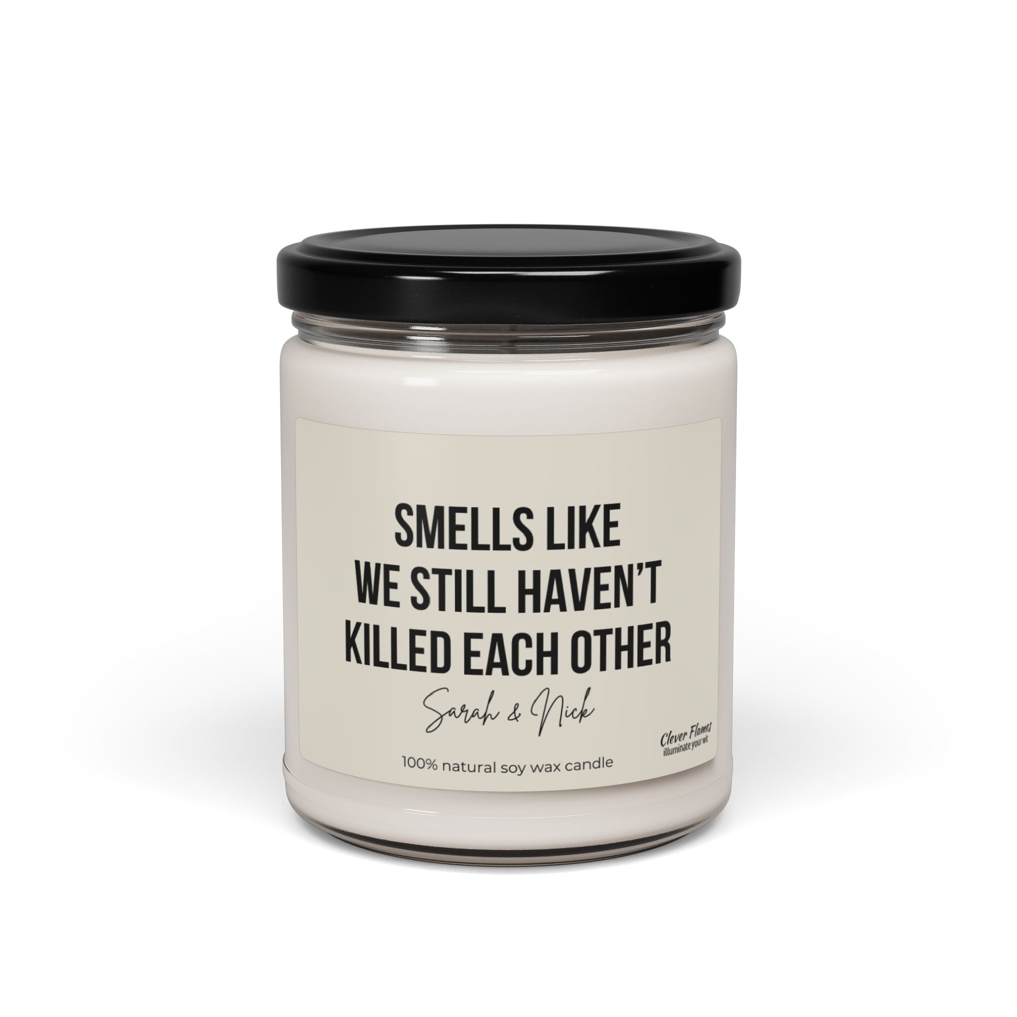 A personalized anniversary candle by Wedding, featuring a humorous message that reads "Smells like we still haven’t killed each other," is crafted from 100% natural soy wax. This white candle comes in a glass jar with a black lid and makes an excellent gift for friends, husbands, wives, birthdays, or Valentine's Day.
