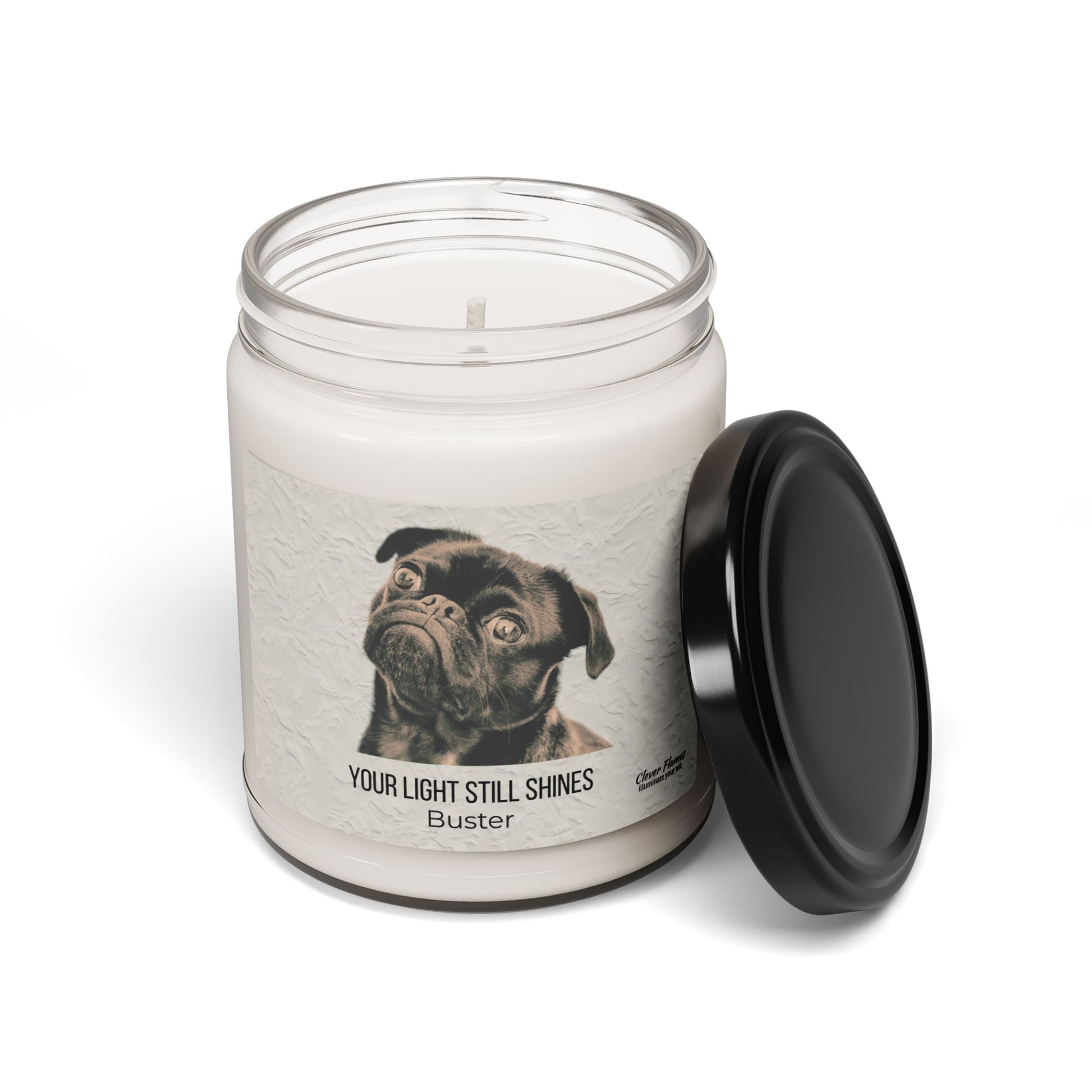 The Printify Your Light Still Shines Personalized Pet Memorial Candle is a white candle in a glass jar with a black lid, featuring a label with a black pug drawing—a heartfelt sympathy and remembrance gift for pet lovers.