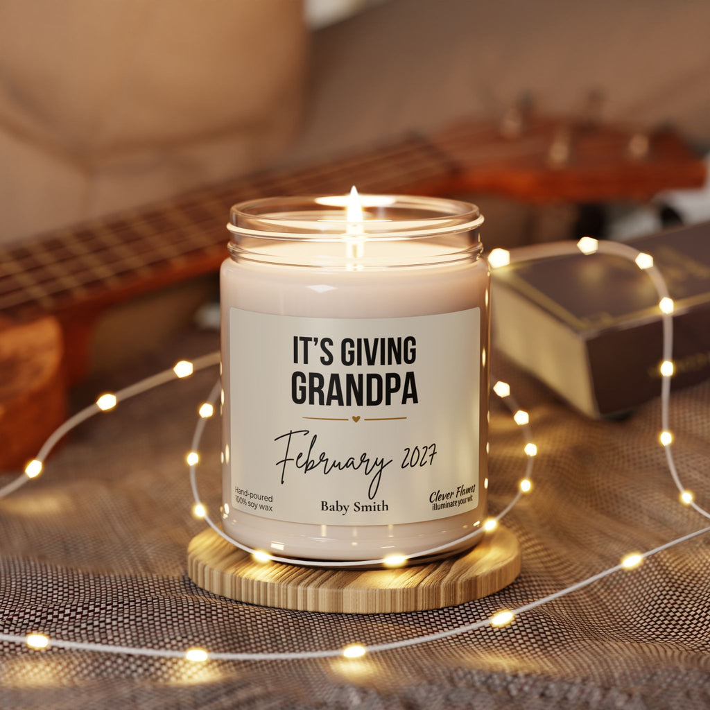 A Grandpa Pregnancy Announcement Candle in a glass jar reading Its giving Grandpa, February 2027, Baby Smith, sitting on a wooden coaster surrounded by string lights.
