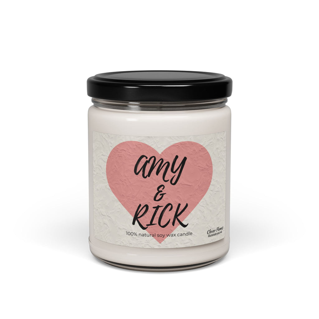 A white candle in a glass jar with a black lid features a pink heart labeled Amy & Rick in bold script. Below, it reads 100% natural soy wax candle. This Printify Personalized Couples Candle is an ideal romantic gift for Valentines Day or anniversaries.