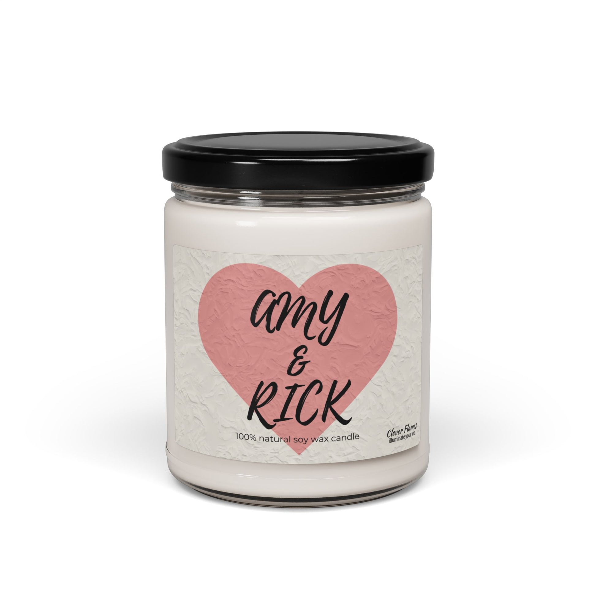 A white candle in a glass jar with a black lid features a pink heart labeled Amy & Rick in bold script. Below, it reads 100% natural soy wax candle. This Printify Personalized Couples Candle is an ideal romantic gift for Valentines Day or anniversaries.