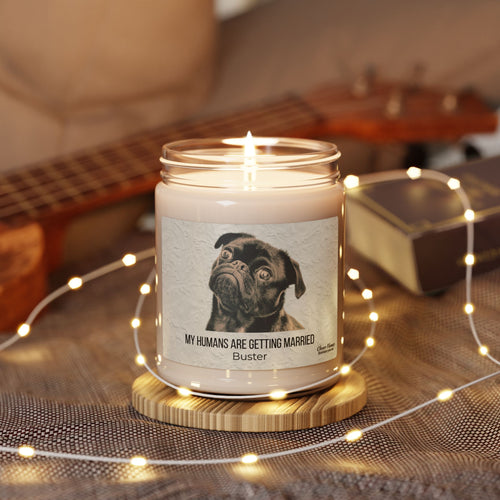 The My Humans Are Getting Married Personalized Pet Engagement Candle by Printify features a custom label with a pug and sits in a glass jar on a wooden coaster—ideal as an engagement gift for pet lovers.