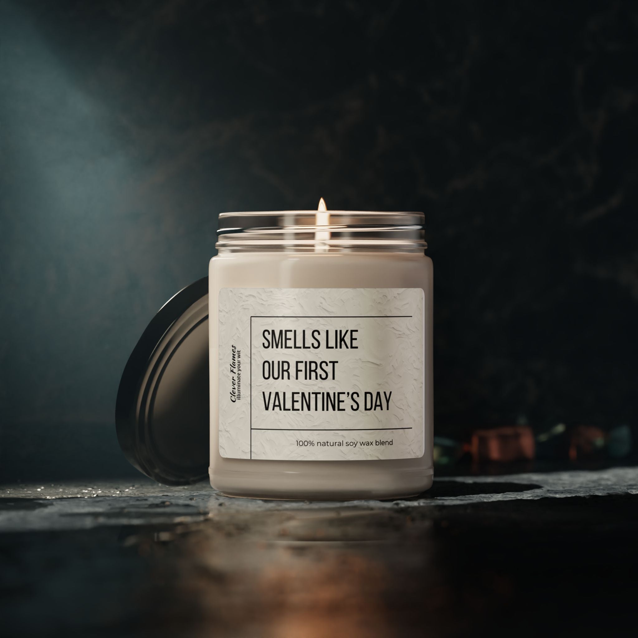 The Printify Smells Like Our First Valentines Day – Personalized Romantic Candle, Custom Couples Gift sits elegantly on a textured surface against a dark background. The lit soy wax candle with its lid beside it features an inscribed romantic label.