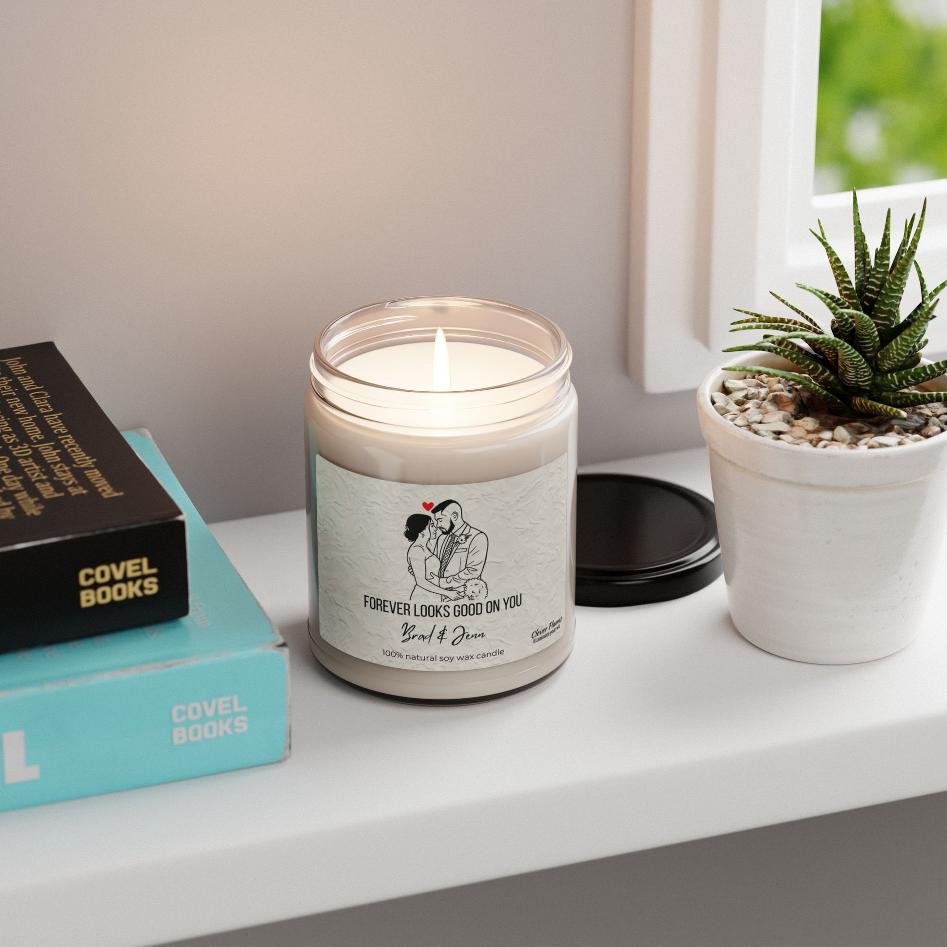 The Printify Custom Couple Candle, a soy wax personalized wedding gift with couple line art and “Forever looks good on you” label, sits in a glass jar on a white shelf beside a succulent and books—perfect for anniversaries or Valentine’s.