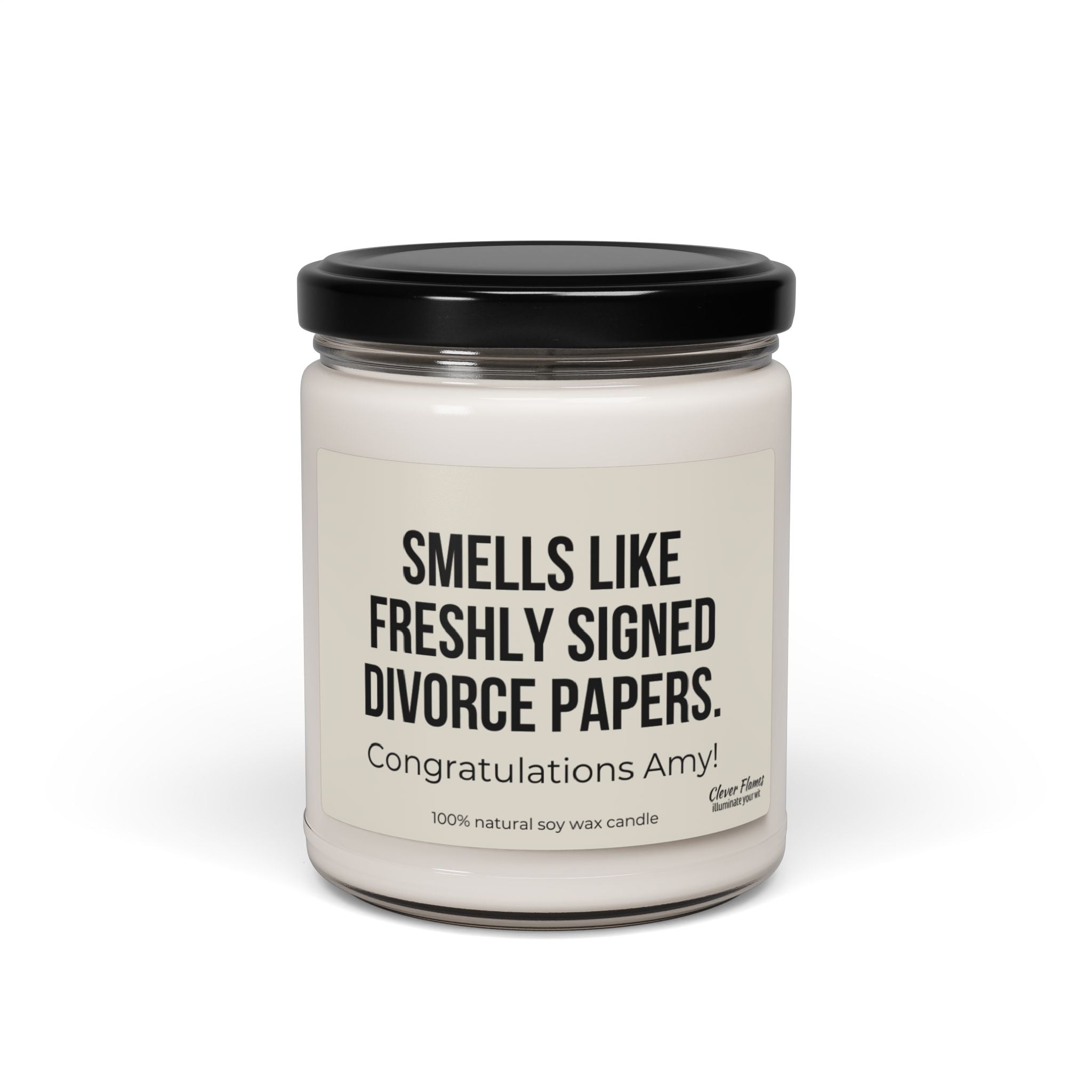 A Printify personalized soy candle comes in a glass jar with a black lid, featuring the label, "Smells Like Freshly Signed Divorce Papers. Congratulations Amy!" This 100% natural soy wax candle is the perfect funny gift for a divorce party.