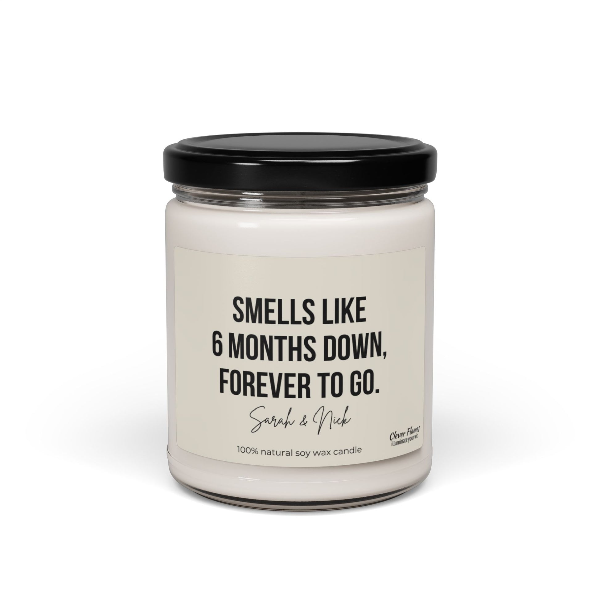 A personalized 6-month anniversary candle, crafted by Wedding from 100% natural soy wax, showcases a white jar with a black lid featuring the text: Smells like 6 months down, forever to go. Sarah & Nick. It's an ideal gift for friends or partners and adds a memorable, fragrant touch to any celebration.