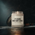 A personalized candle from Printify, featuring soy wax in a glass jar, emits a warm glow. The label reads "Great Aunt and Uncle Pregnancy Announcement Candle Due June 2025," beautifully setting an intimate scene with its dark background, leaf accents, and wooden surface. This baby announcement gift is the perfect way to reveal your joyful news to a great aunt and uncle.