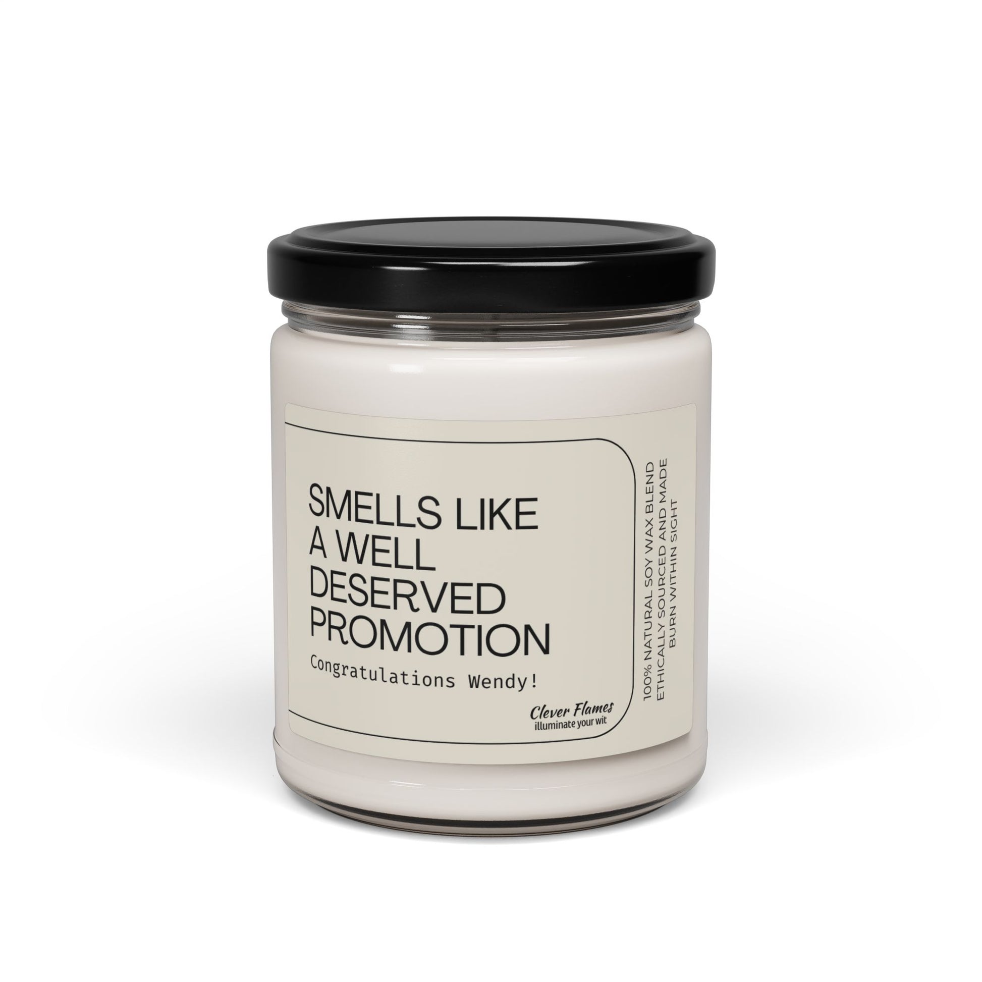 The Smells Like a Well Deserved Promotion personalized soy wax candle by Printify features a white, clean-burning wax in a glass jar with a black lid. The custom label reads: Congratulations Wendy! Photographed on a white background.
