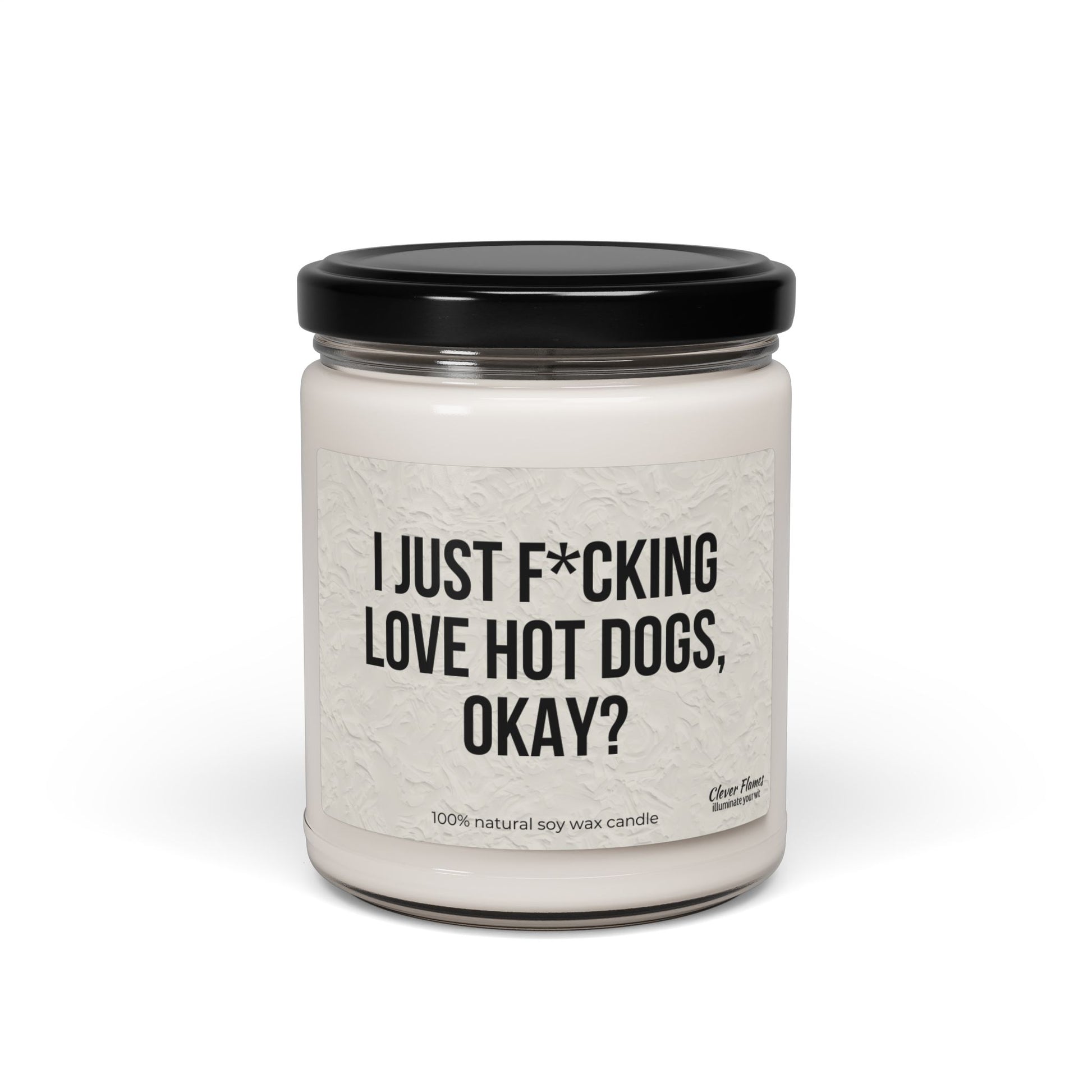 The Printify "I Just F*cking Love Hot Dogs Okay?" Candle is a 9oz white, non-toxic scented soy candle in a reusable glass jar with black lid, featuring a label that reads the product name. Made from 100% natural soy wax.