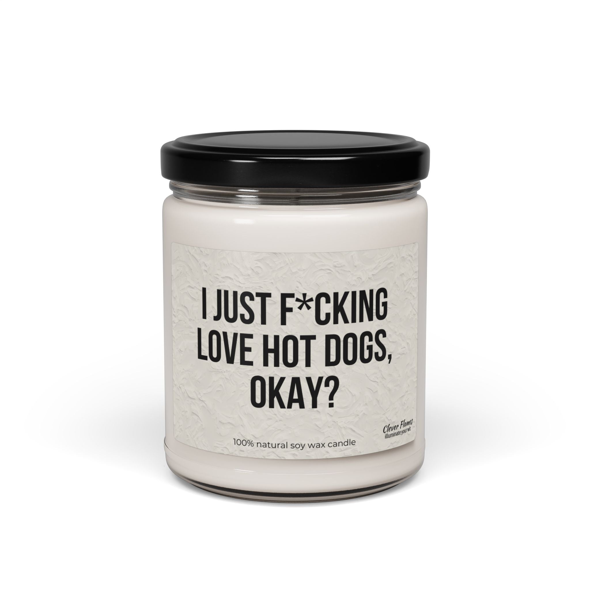 The Printify "I Just F*cking Love Hot Dogs Okay?" Candle is a 9oz white, non-toxic scented soy candle in a reusable glass jar with black lid, featuring a label that reads the product name. Made from 100% natural soy wax.