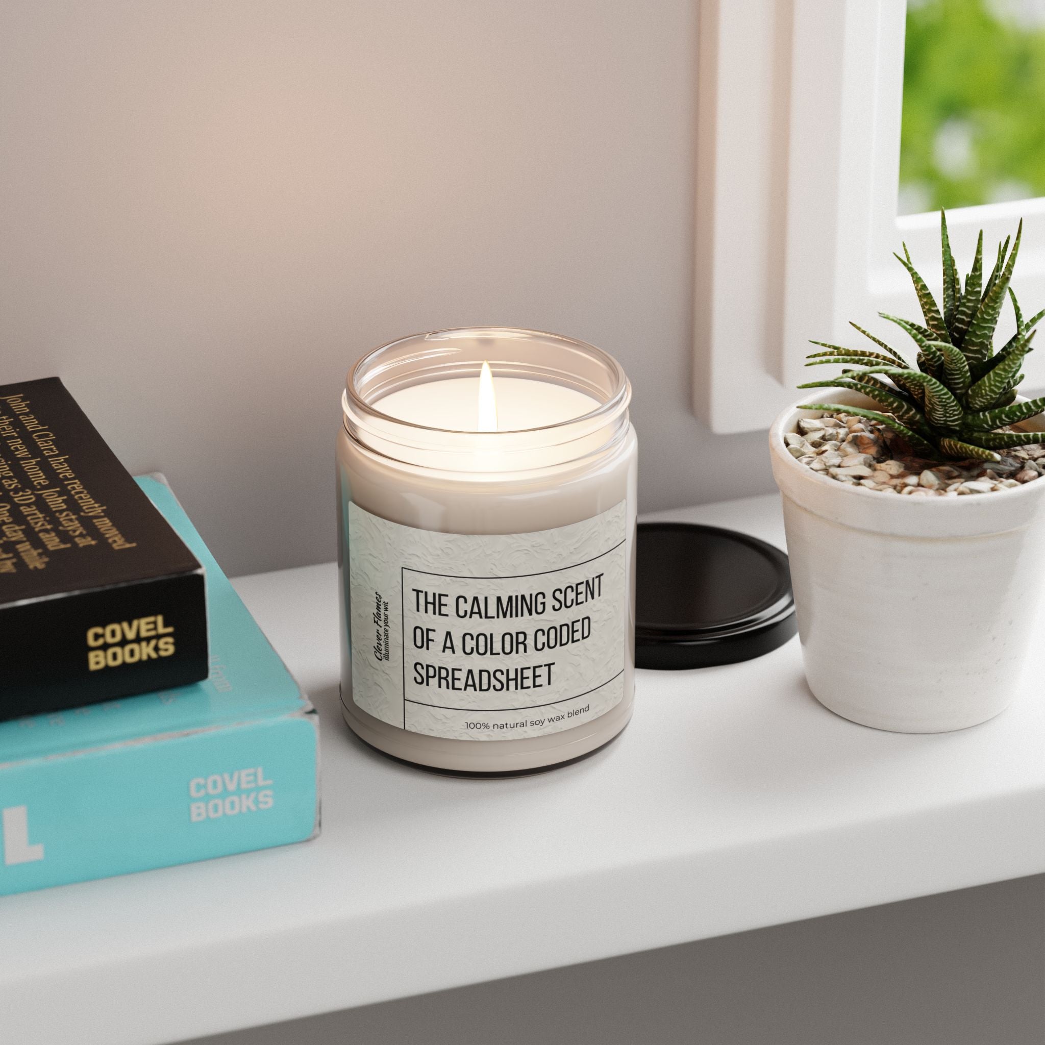 The Scented Soy Candle - The Calming Scent of a Color Coded Spreadsheet by Printify rests on a white shelf beside two books, a black book, and a small potted succulent—ideal for eco-friendly home fragrance lovers.