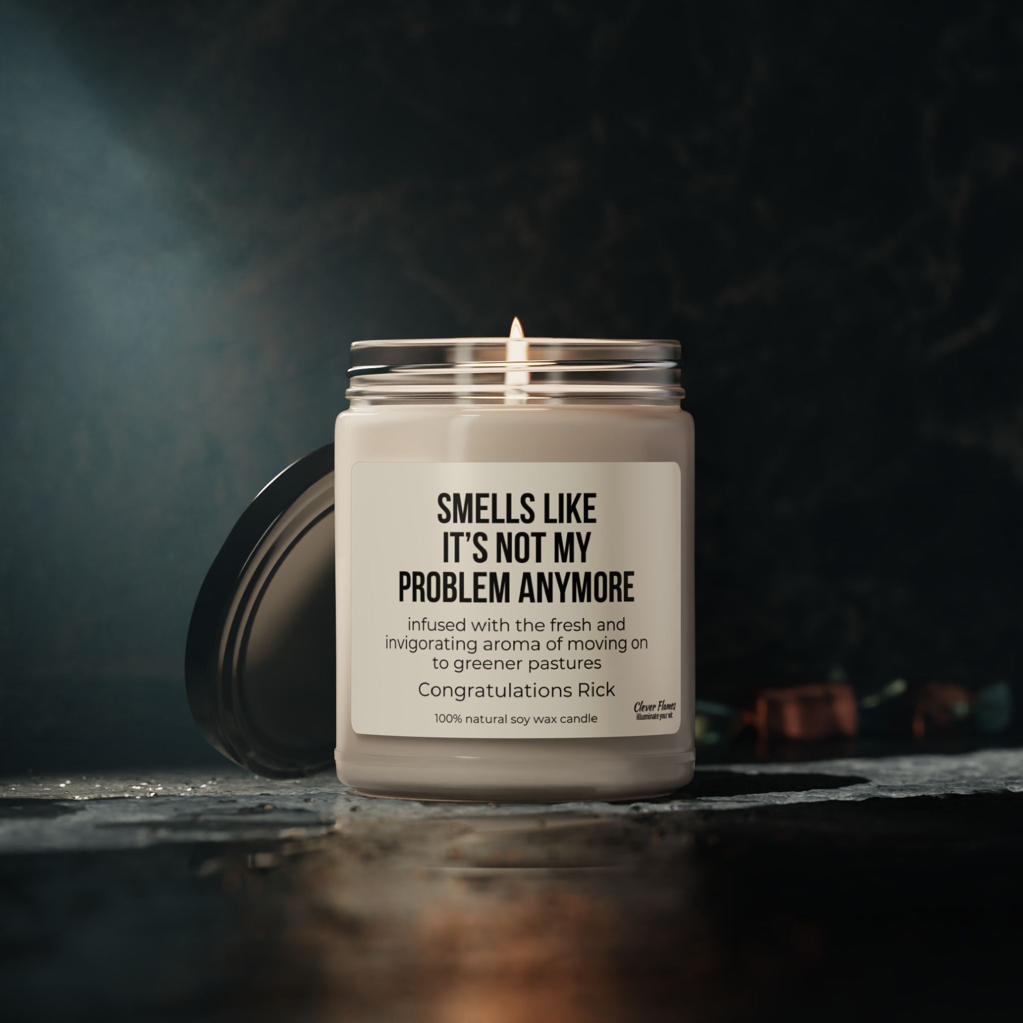 A soy candle from Printify, placed on a dark surface, features the text: "Smells like it's not my problem anymore." Embodying the fresh and invigorating scent of embracing new opportunities, this personalized retirement candle is a humorous farewell gift. Congratulations, Rick!